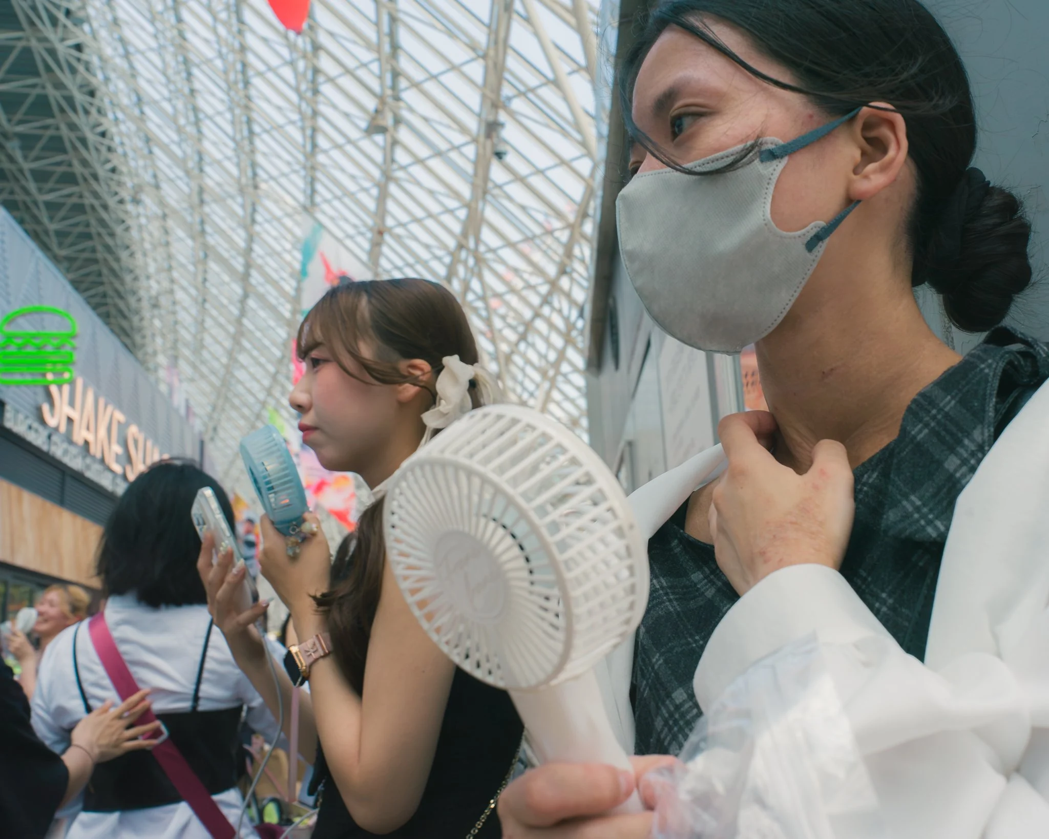 Close-up of two women wearing face masks at an indoor event with a high glass ceiling and structural beams.