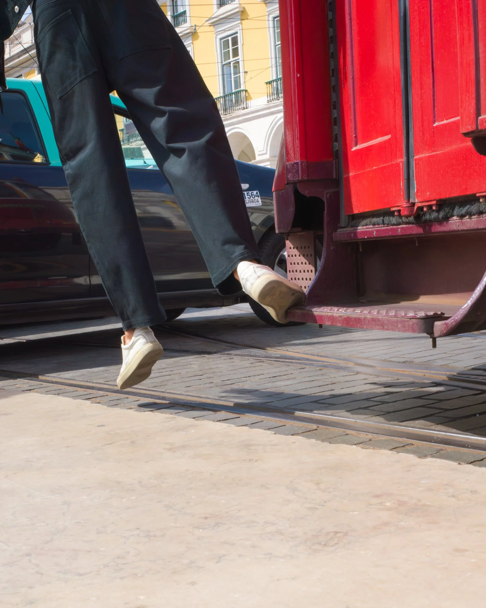 A person wearing black pants and white sneakers stepping off a red cart or vehicle with a city street and buildings in the background.