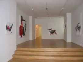 Kunstwerke in einer Galerie, Wandbilder mit abstrakten Designs, weiße Wände, Holzbohlenboden, gut beleuchteter Raum.