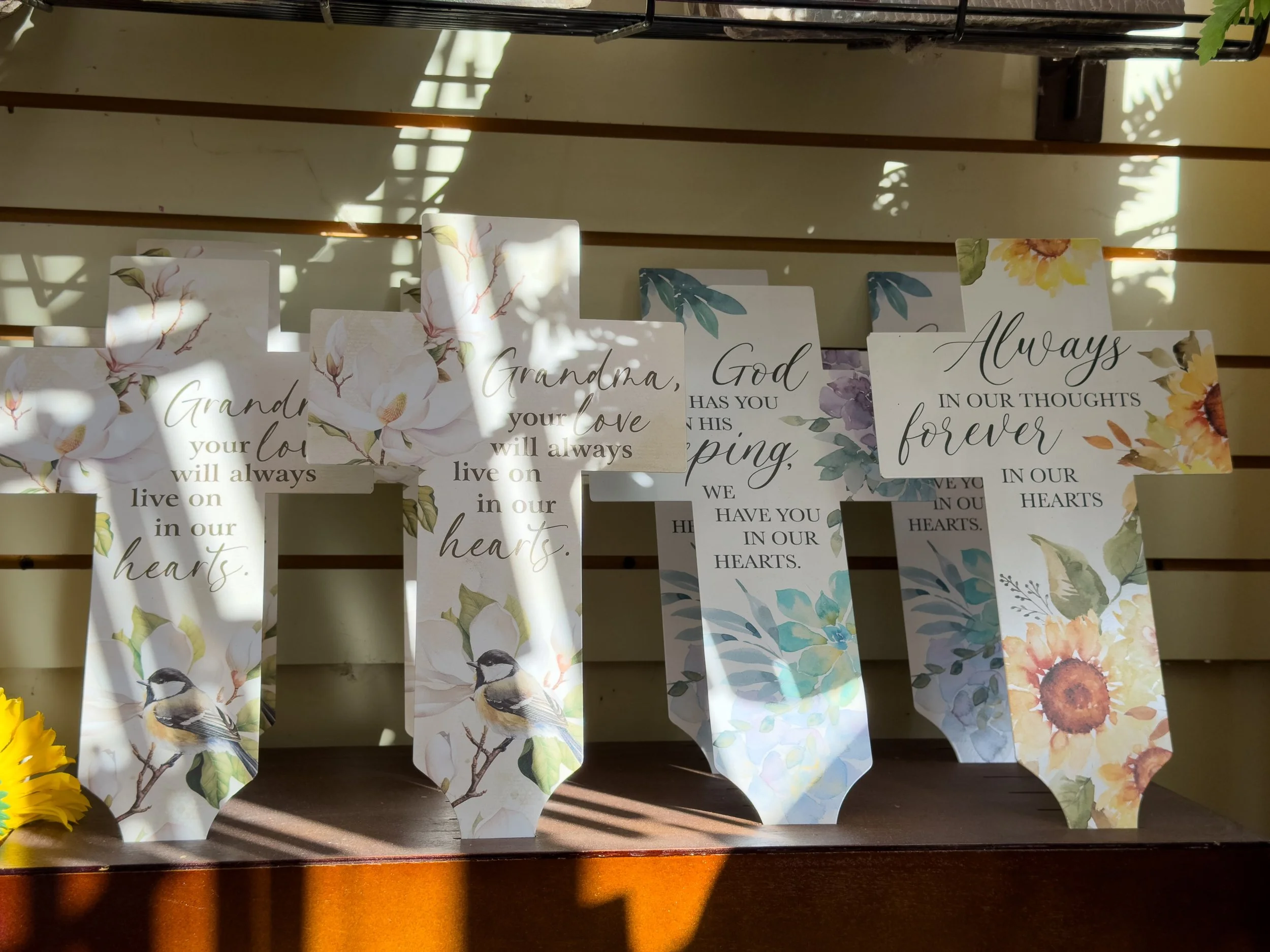 Decorative plaques with floral and bird designs and inspirational quotes, displayed on a wooden surface with sunlight and shadows.