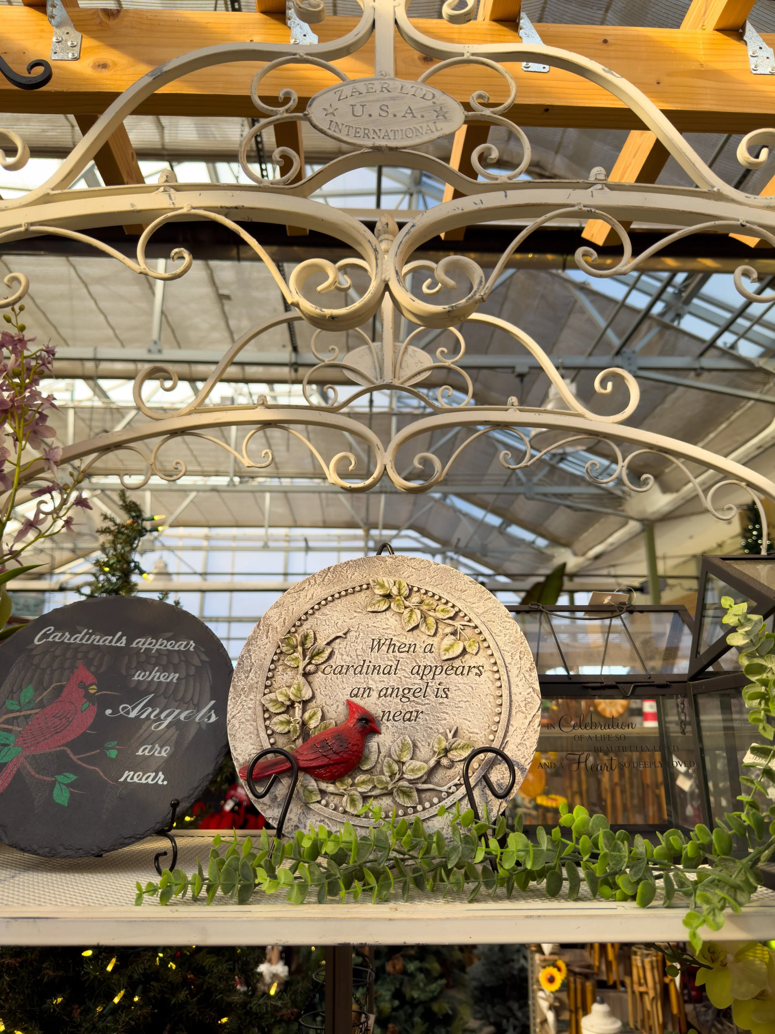 Decorative garden ornaments with cardinal bird designs, including a circular plaque with the quote "When a cardinal appears an angel is near" and another plaque with a cardinal and the quote "Cardinals appear when angels are near" in a greenhouse set