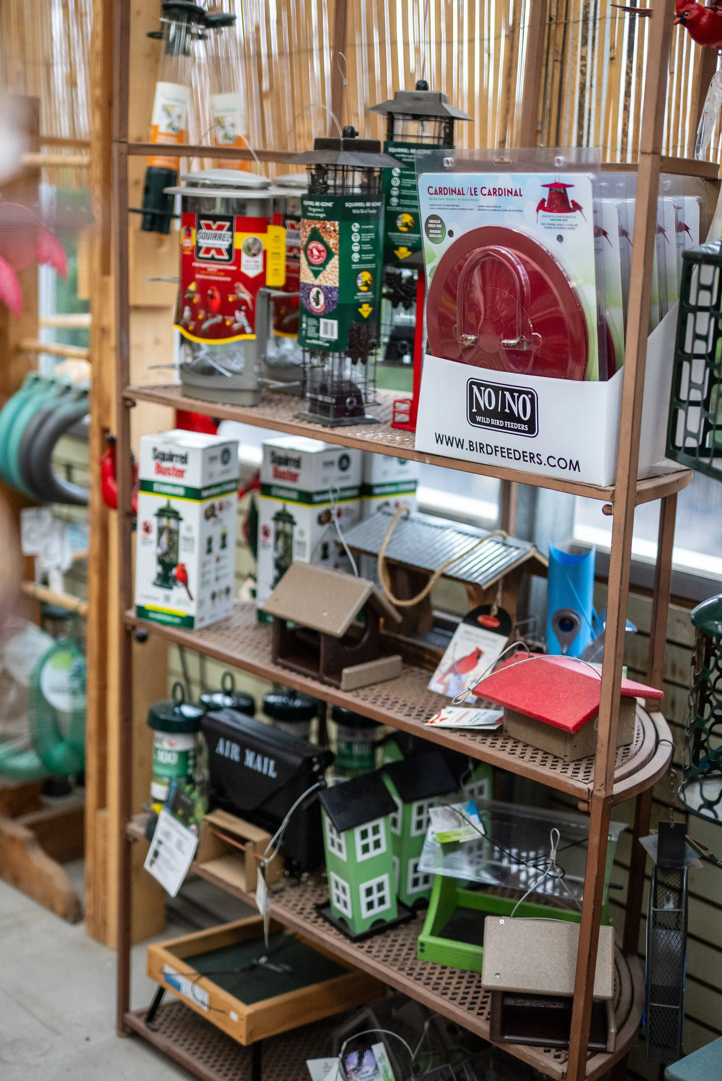 Display of bird feeders and birdhouses on a metal shelf in a store, with various styles and packages visible.