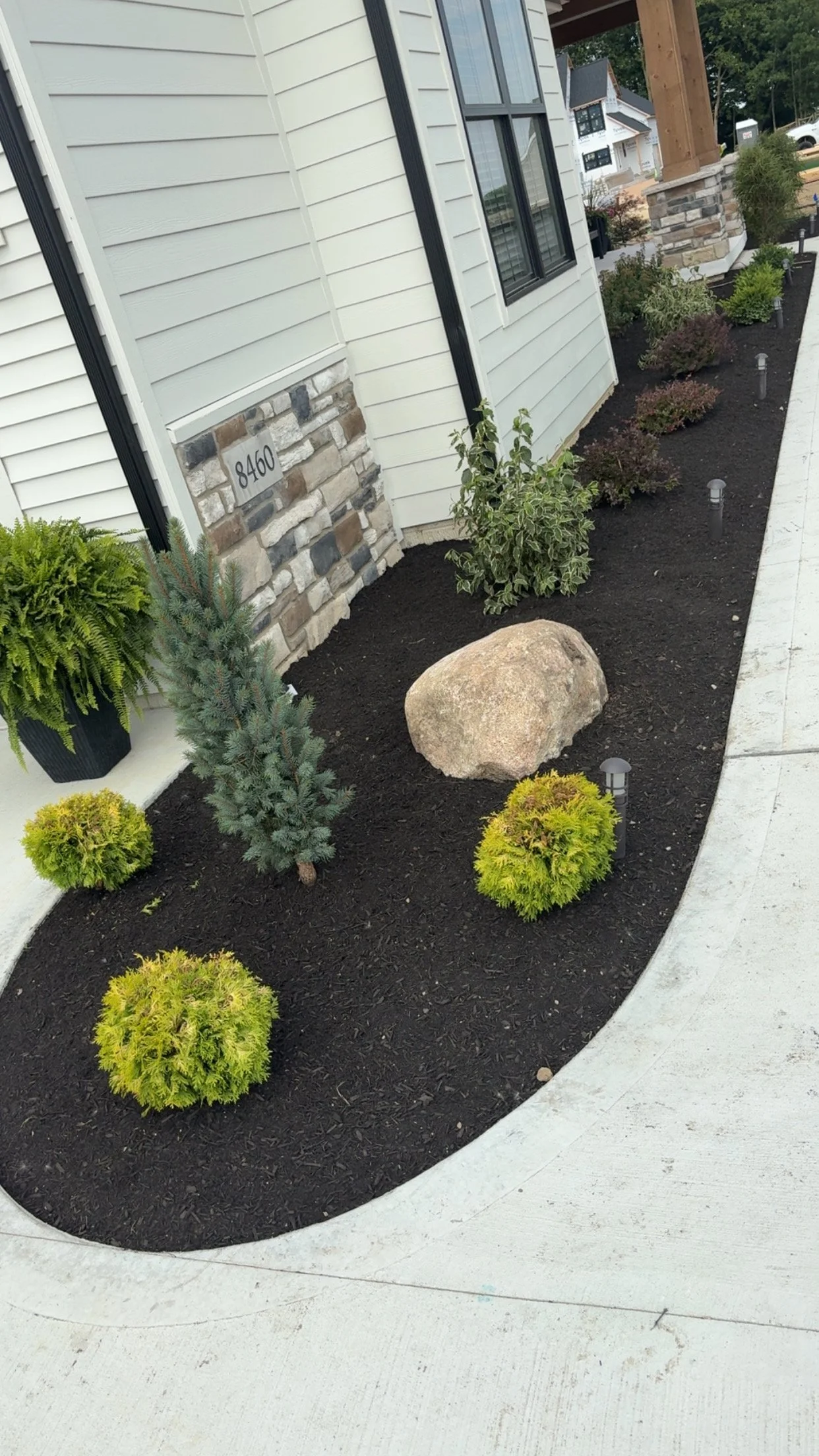 A modern two-story house with black and white exterior, brick accents at the base, attached garage, front porch, green lawn, and concrete driveway.