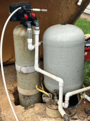 Outdoor water filtration system with two large cylindrical tanks and white PVC pipes