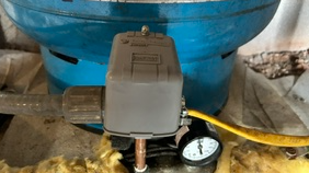 Close-up of a water timer with a pressure gauge, connected to a garden hose, in a garden setting.