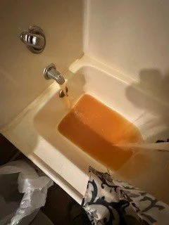 Bathtub containing orange-brown water beneath the tub spout.