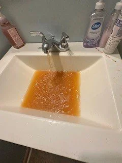 Running faucet filling a white bathroom sink with orange-brown water.