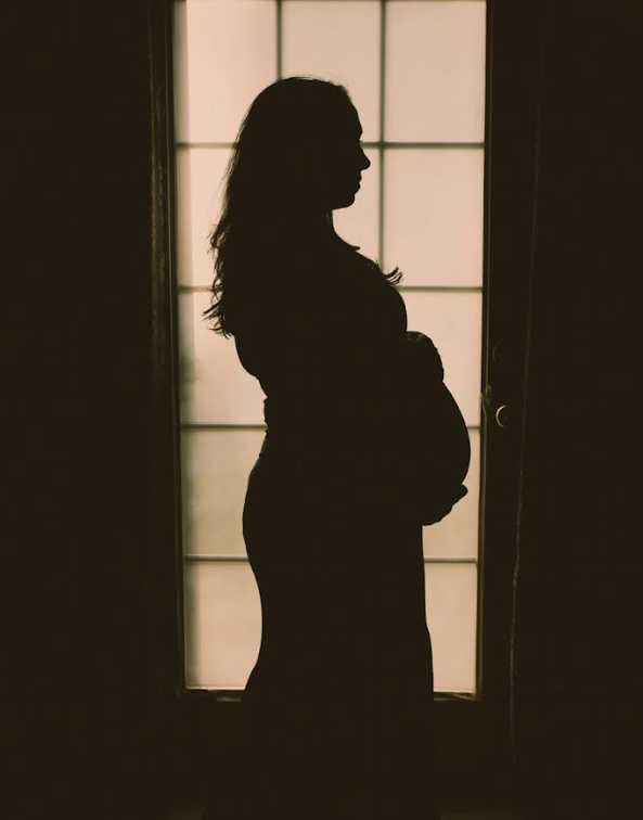 Silhouette of a pregnant woman standing in front of a lit window.
