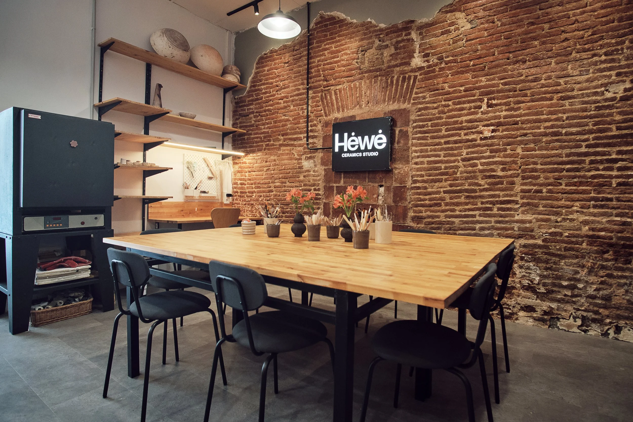 Interior del taller de cerámica Hėwė Studio en Sants, Barcelona, con mesa de trabajo, estanterías y horno