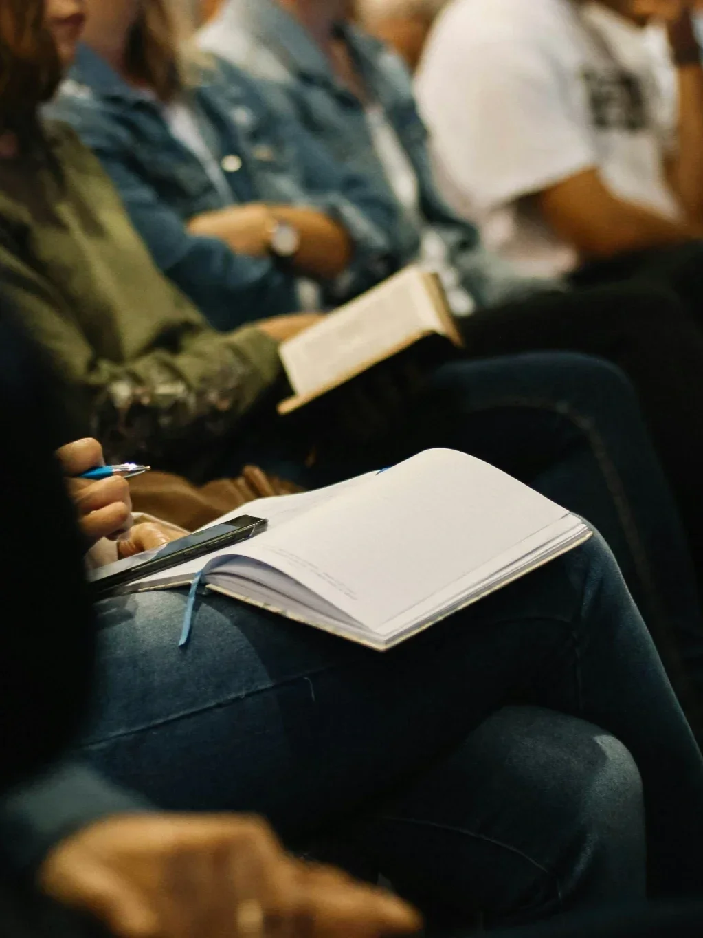 People sitting, taking notes and reading notebooks and papers in a classroom or conference setting.