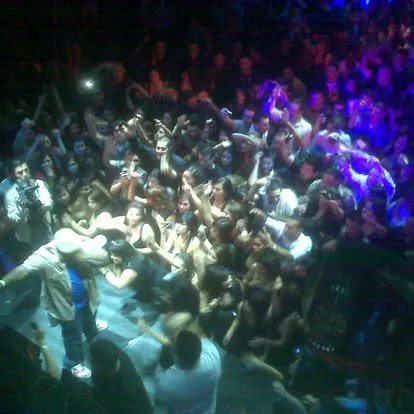 Crowd dancing and partying at a nightclub with colorful lighting.