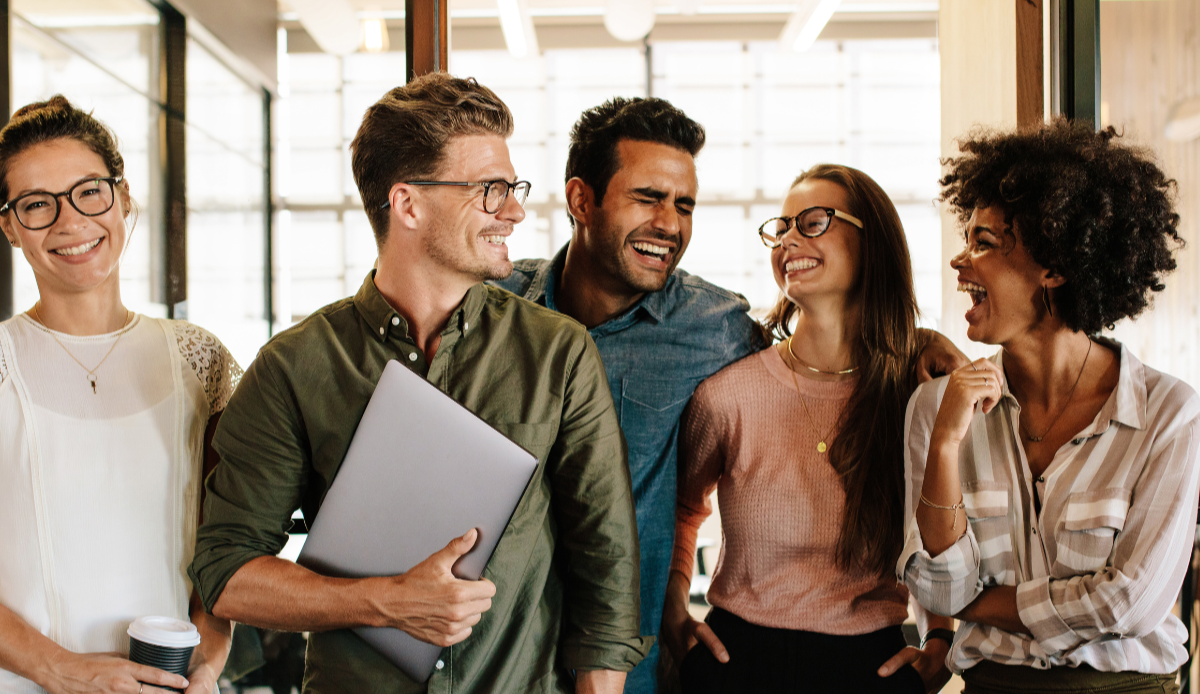 Five diverse young adults laughing and smiling together indoors.