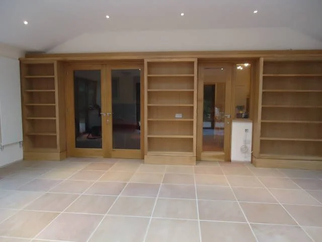 Empty wooden built-in bookshelves with glass door cabinets and tile flooring in a room.