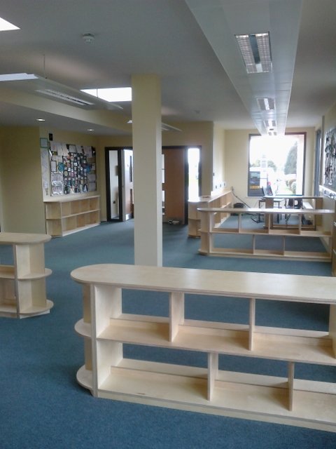 Empty bookstore or library interior with wooden shelves, a bulletin board, and large windows bringing in natural light.