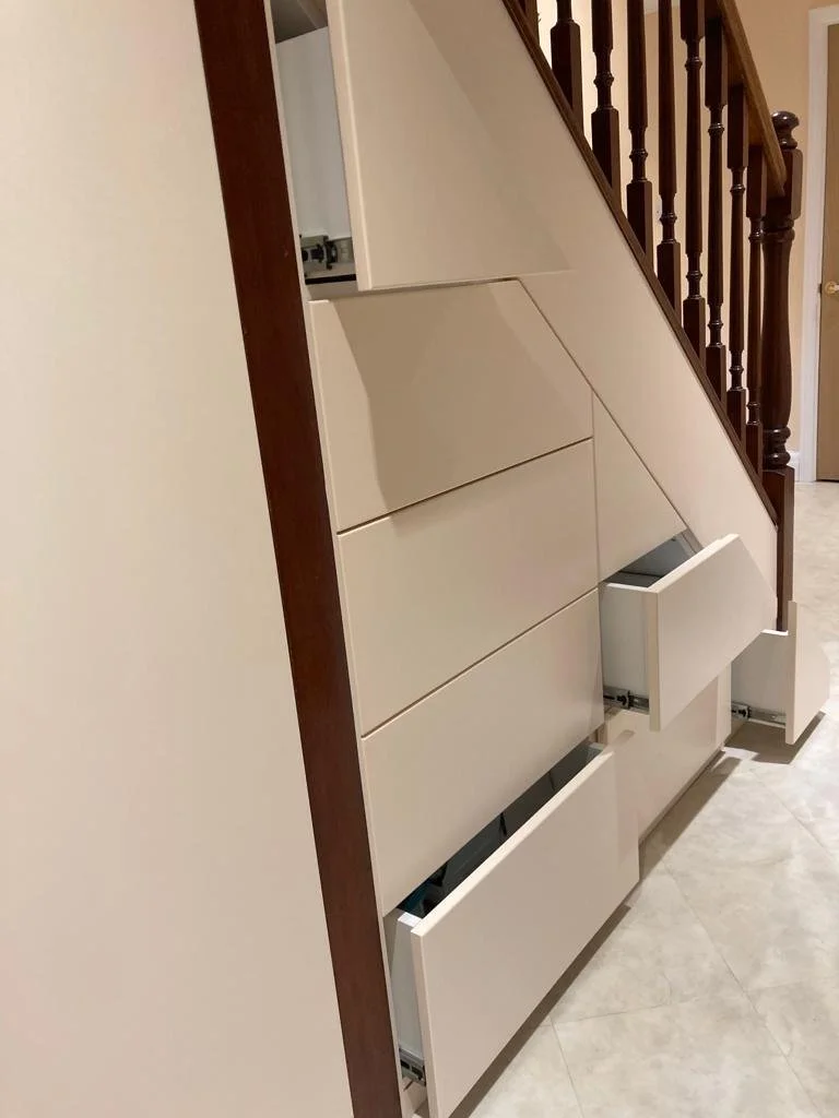 White dresser with multiple open drawers next to staircase with wooden banister.