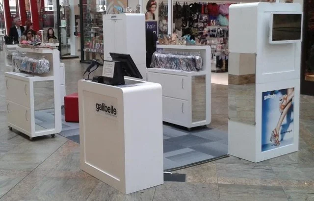 Retail checkout kiosk with a computer monitor and promotional signage in a shopping mall.