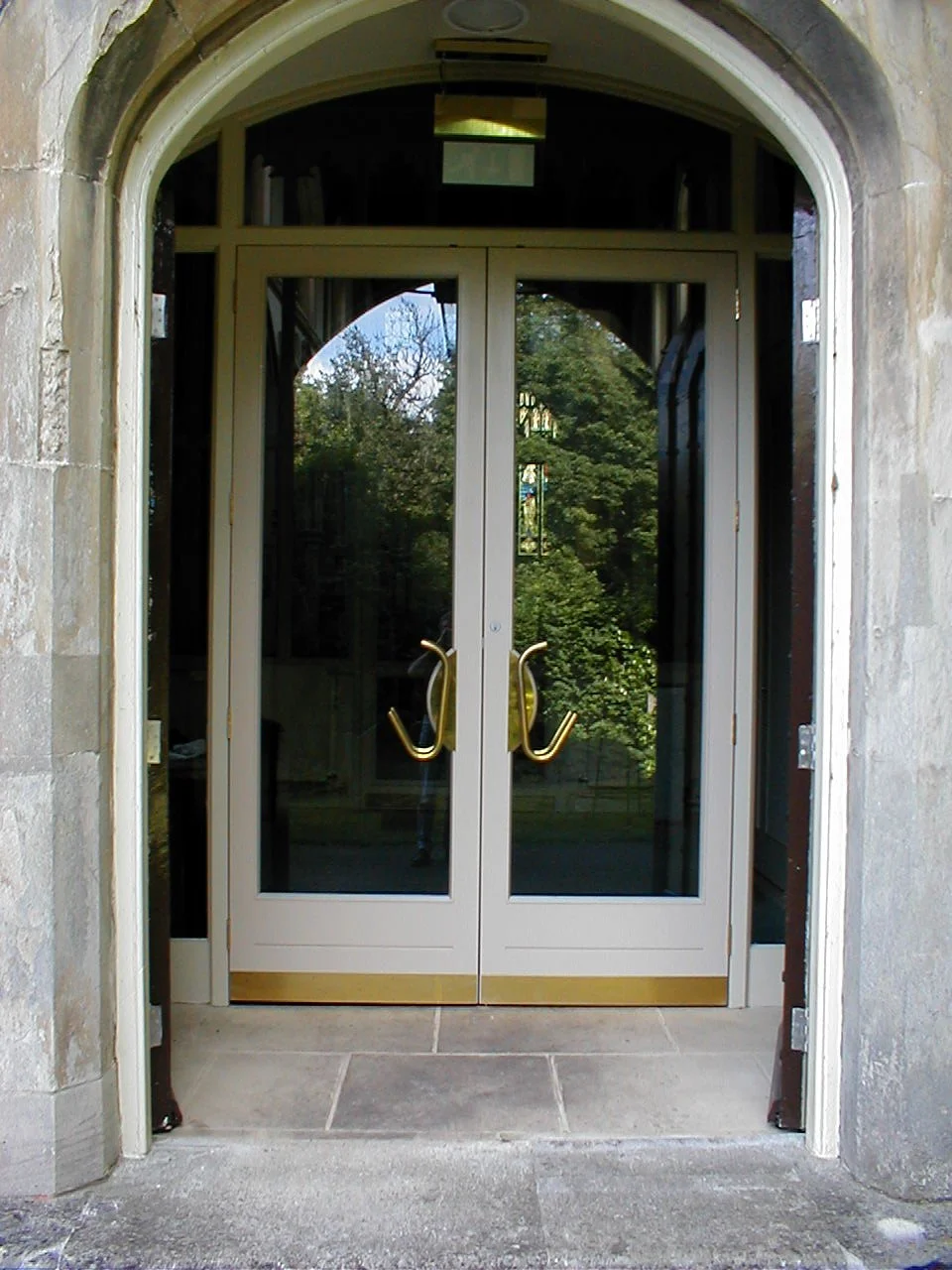Double glass doors with gold handles, set in a stone archway with greenery reflected in the glass.