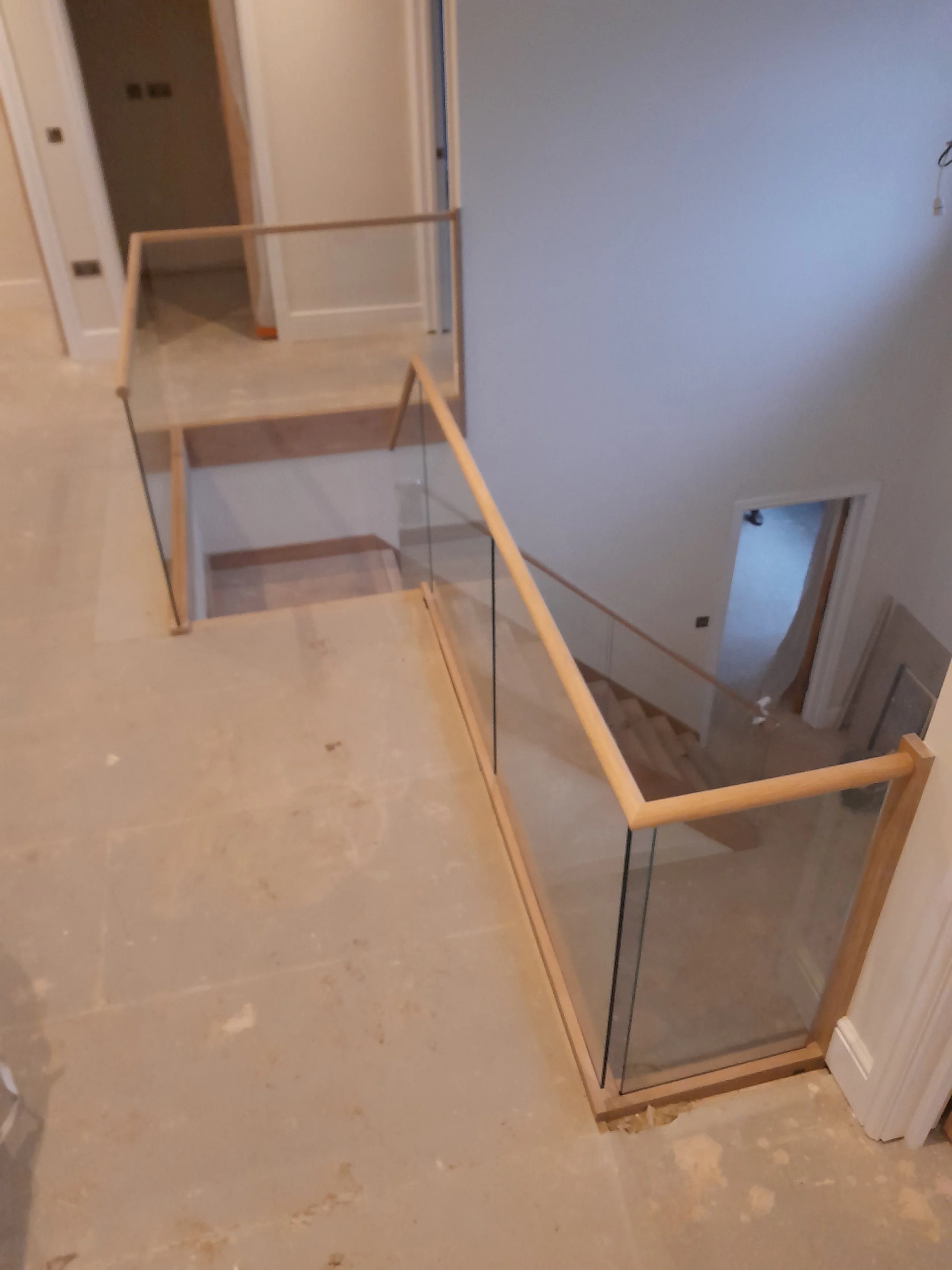 Interior view of a construction site with a glass and wood railing around a staircase opening in a house.