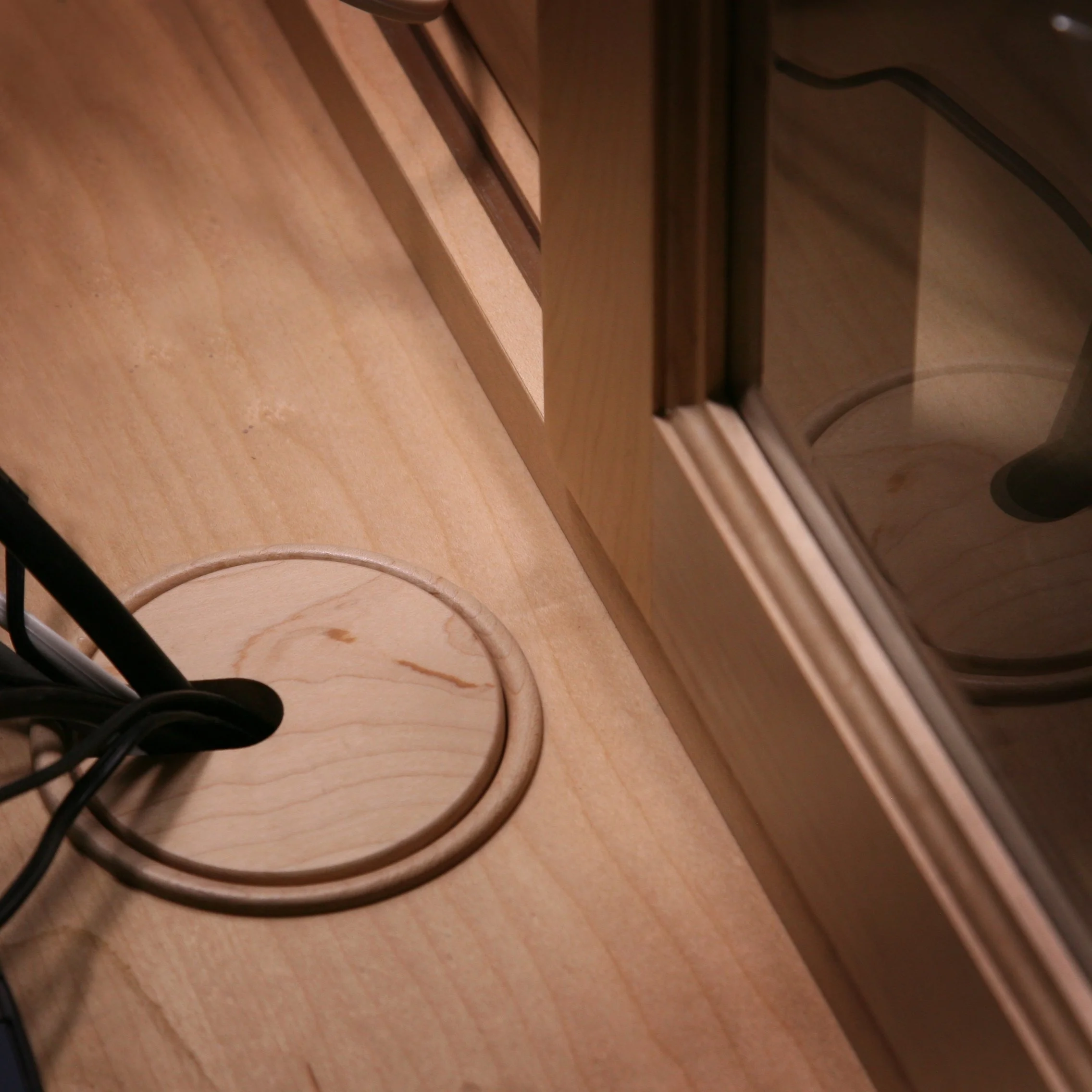 Close-up of a wooden table with a wooden lamp base, electrical cords, and a wooden cabinet or door with a glass panel reflected in a mirror.