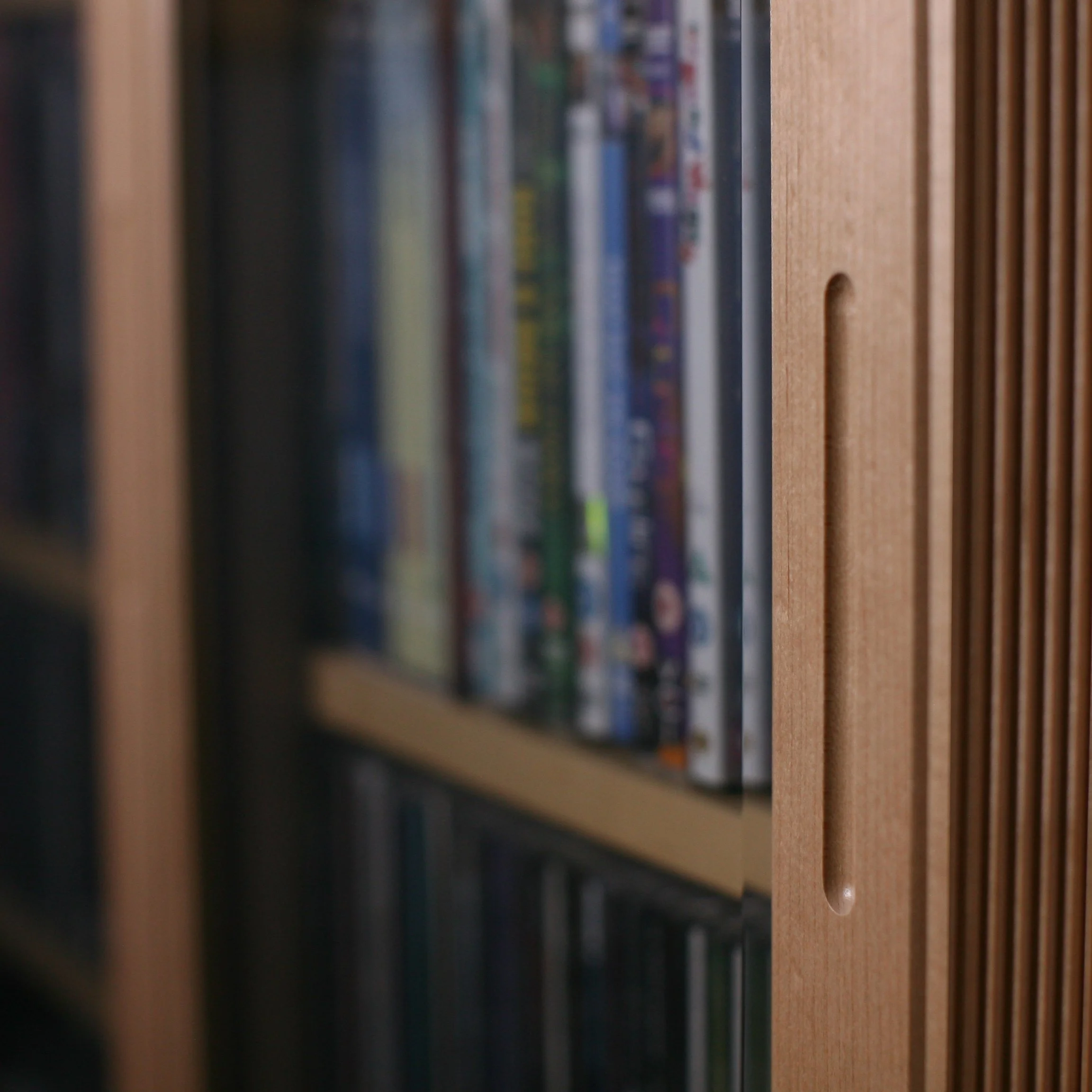 Close-up of a wooden bookshelf with a row of DVDs or video game cases, slightly out of focus.