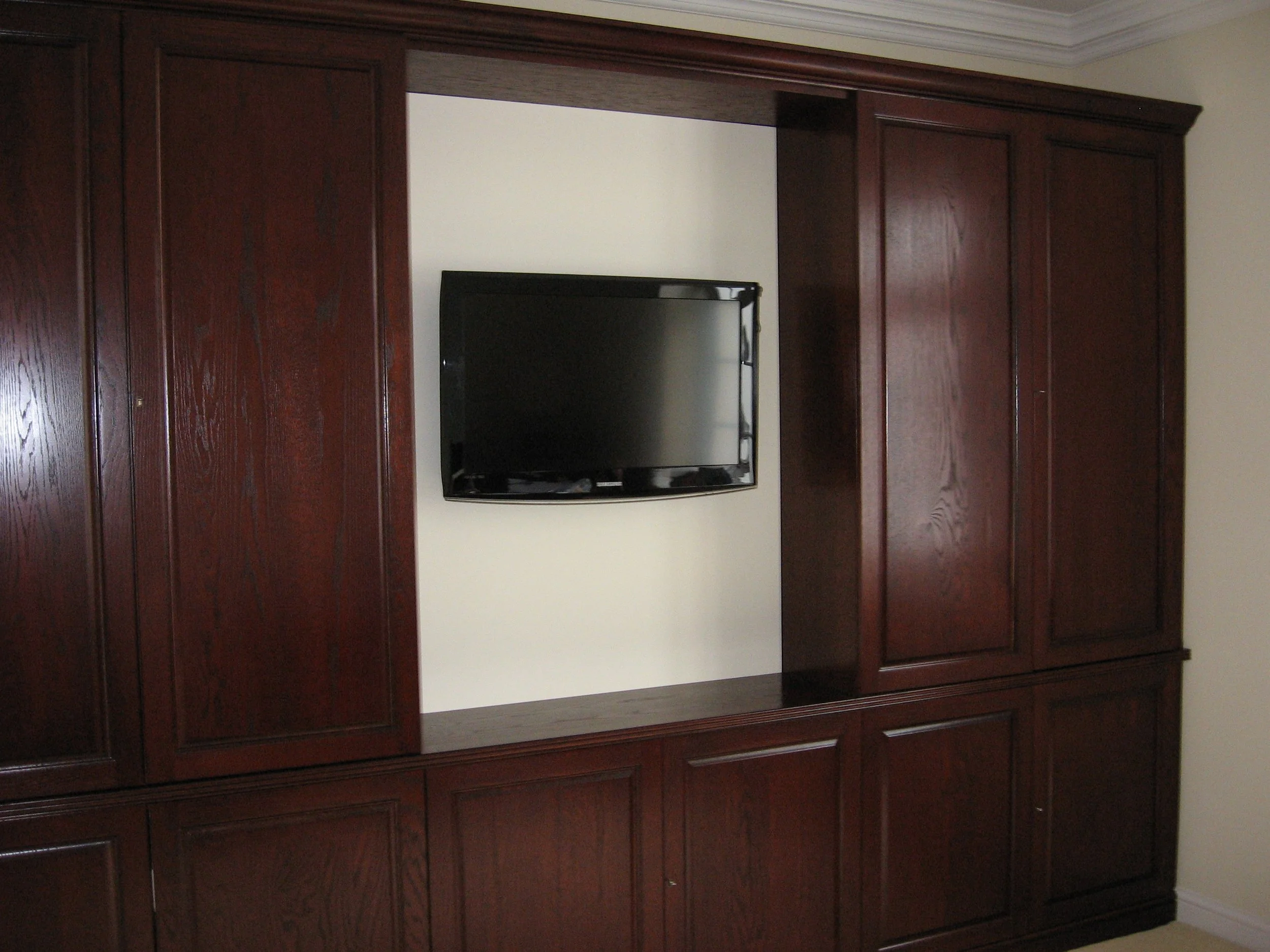 A flat-screen TV mounted on a white wall, surrounded by dark wooden cabinetry.