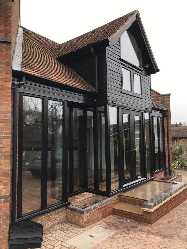 A backyard extension with glass sliding doors, a wooden deck, and a black-painted gabled upper section of the house.