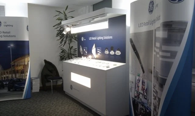 Exhibit booth displaying LED retail lighting solutions with product displays, banners, and promotional materials.