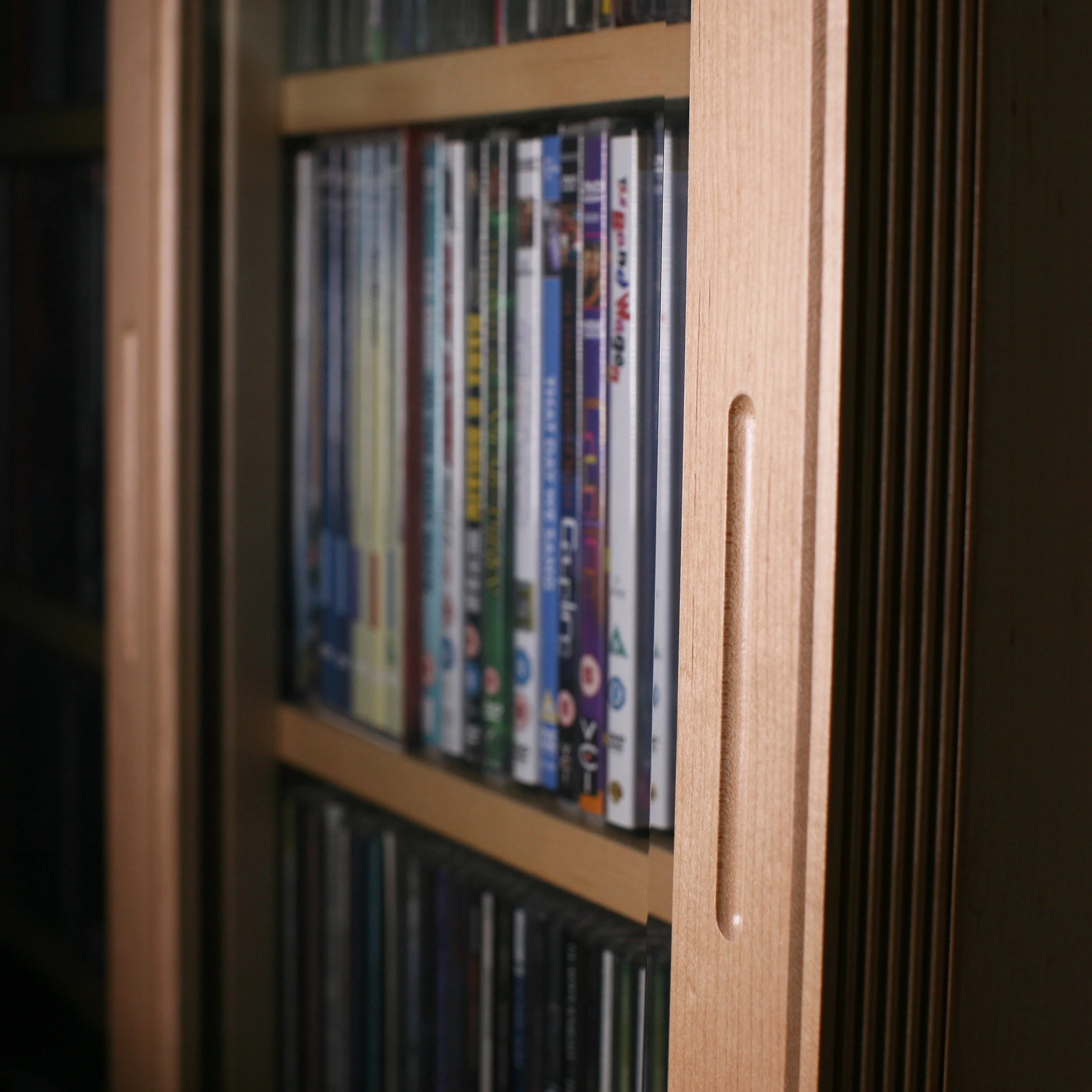 Close-up of a wooden bookshelf filled with DVDs and video games, with a focus on the side of the shelf.