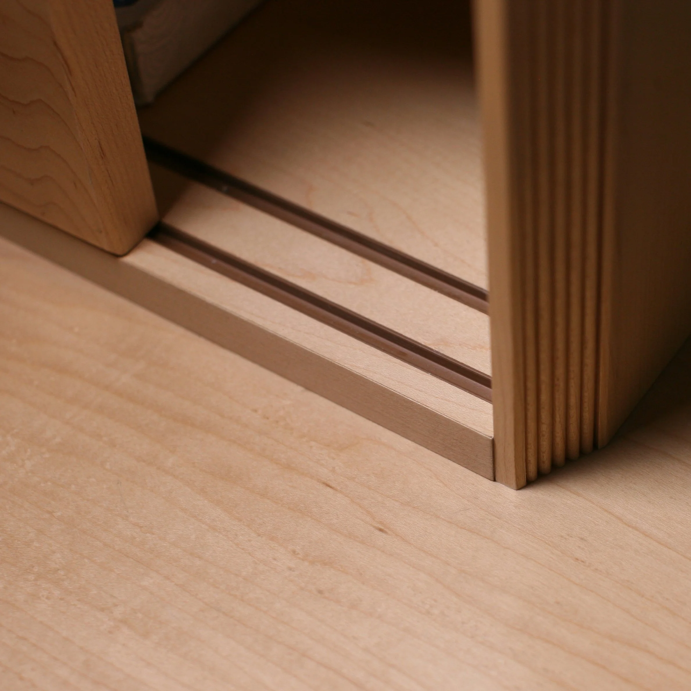 Close-up view of a wooden furniture corner with grooves and a light wood finish on a matching wooden surface.