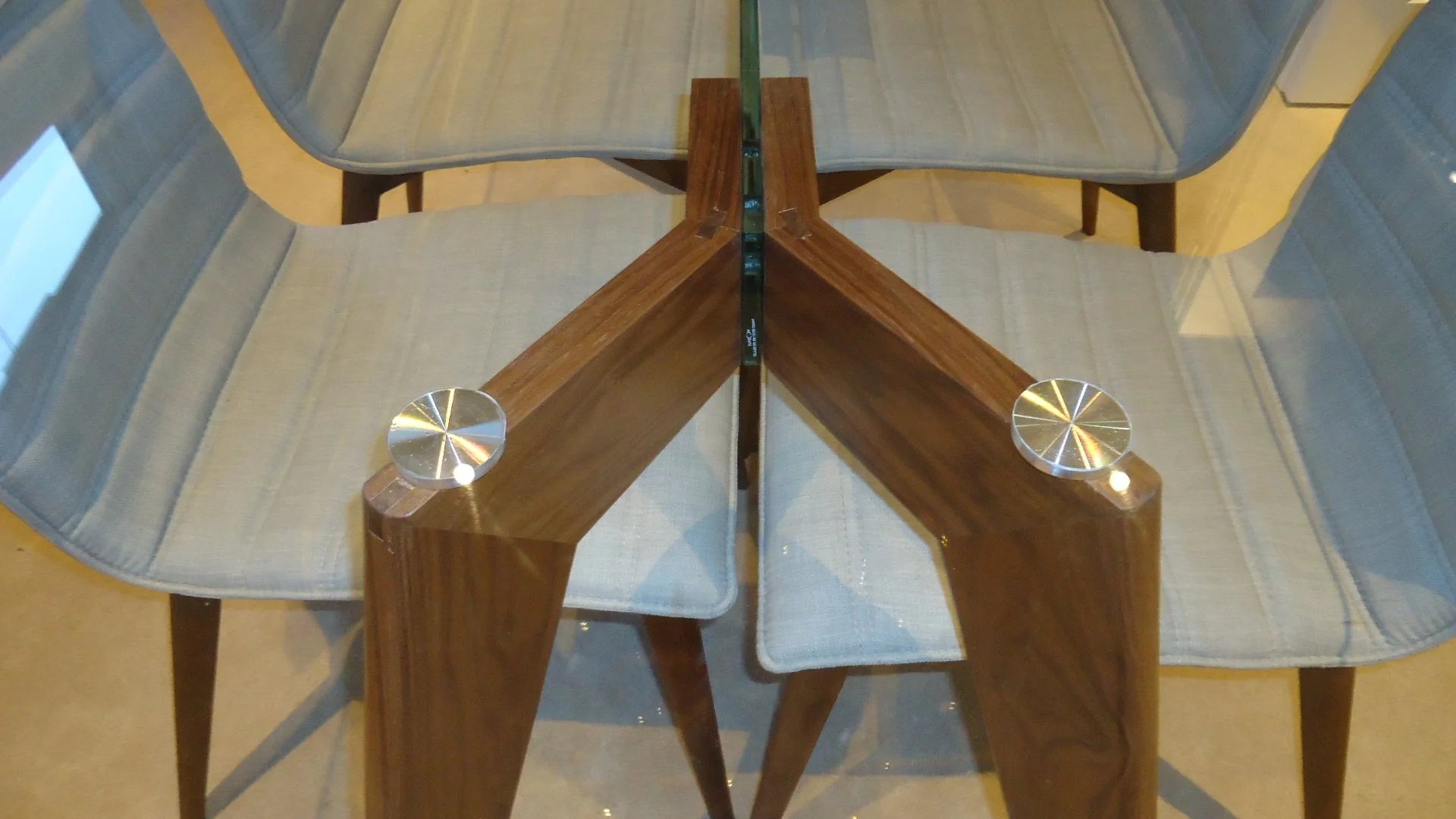 View of a glass-topped wooden table with a central metal support, surrounded by chairs with light gray striped upholstery, showing a symmetrical arrangement.