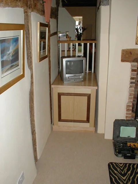 Small hallway with framed artwork on the wall, a vintage TV on a cabinet, and a fireplace on the right. An open door leads to another room in the background.