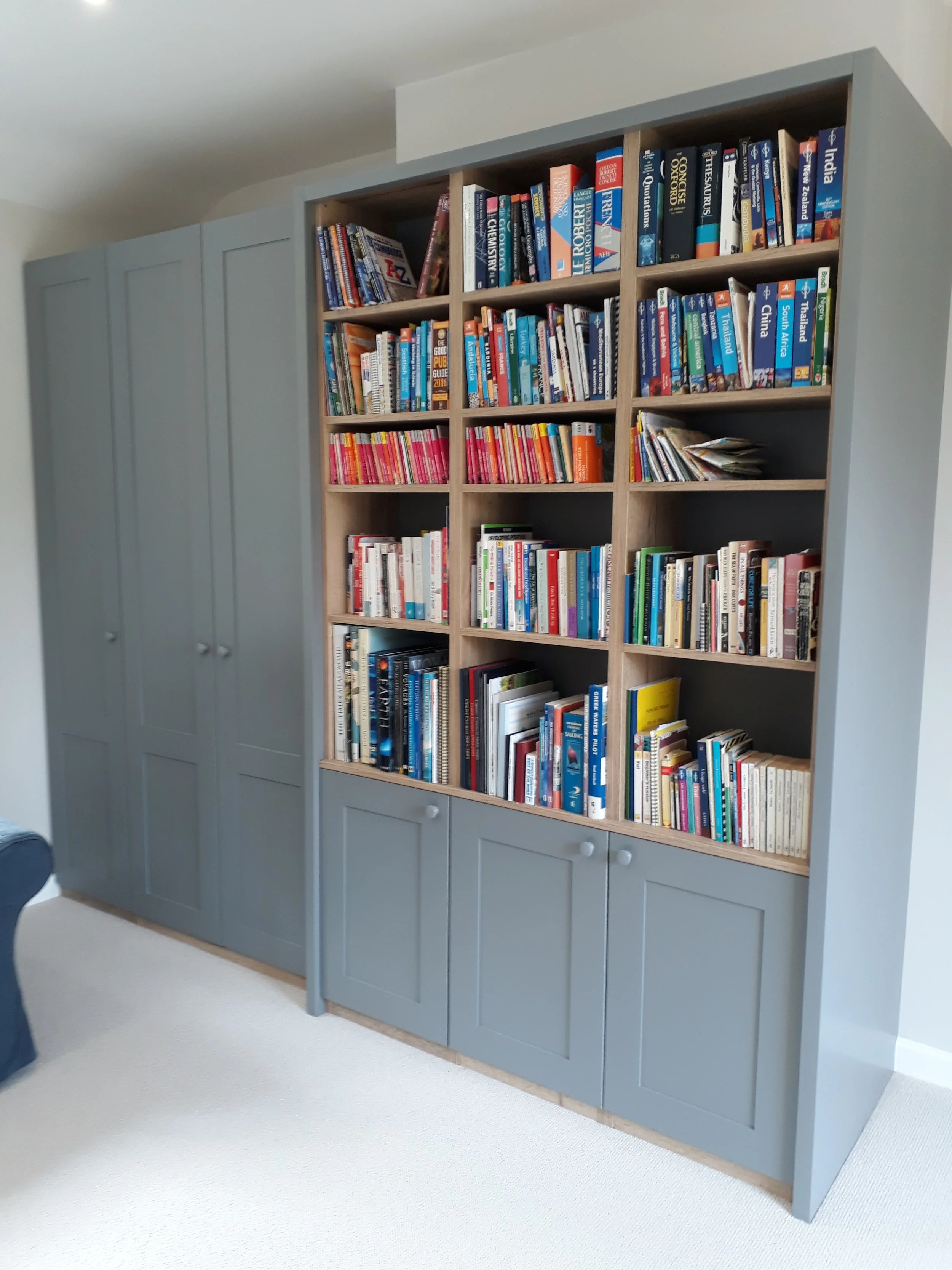 A tall, stacked bookshelf filled with a variety of books, in a room with light-colored walls and carpeting.