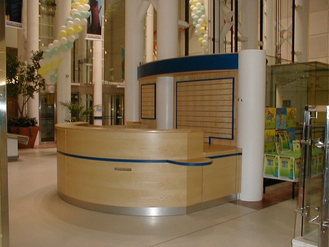 Empty wooden kiosk or booth with blue top trim inside shopping mall or commercial space.