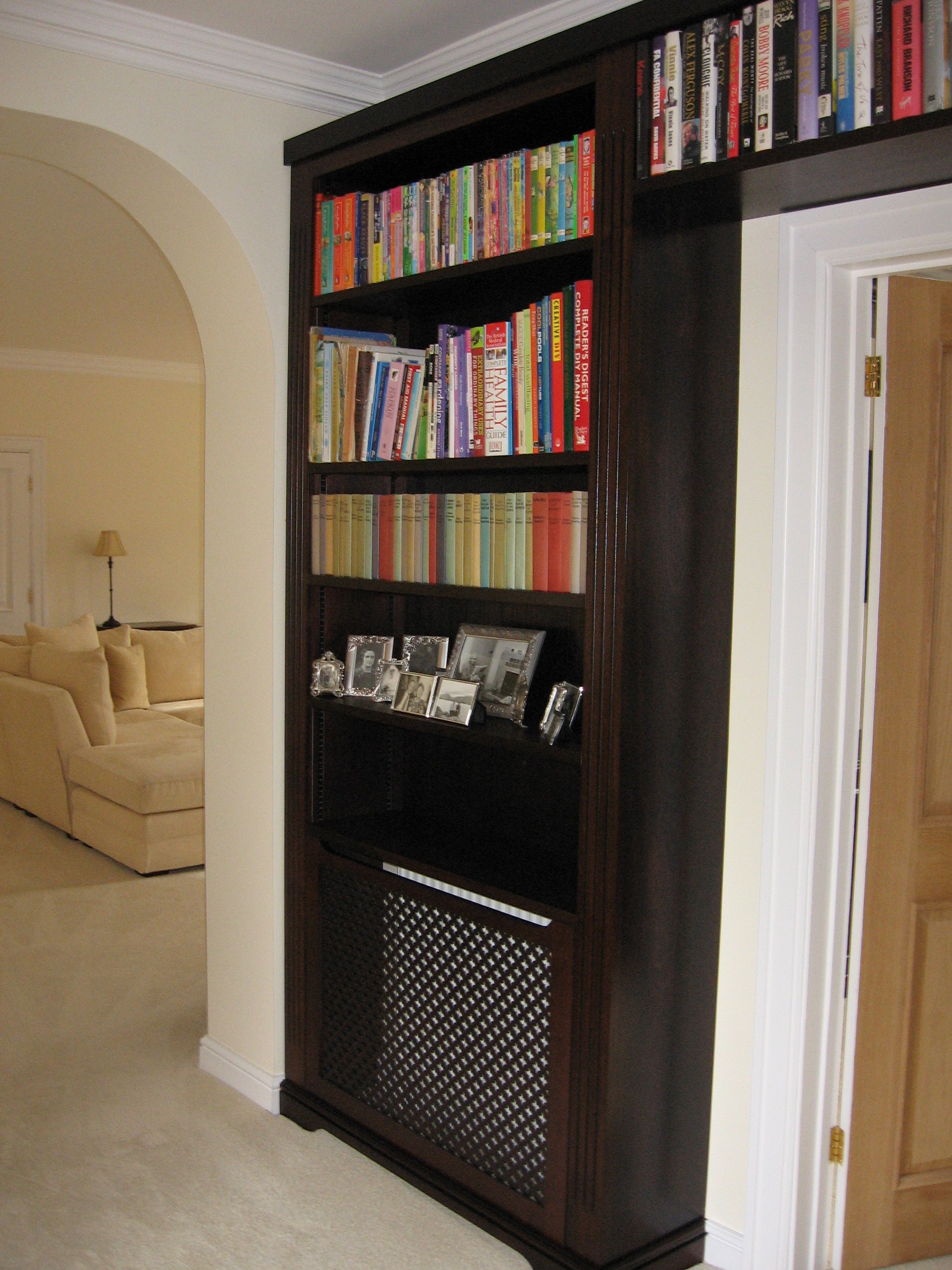 Dark wooden bookshelf filled with colorful books and photographs in a living room.