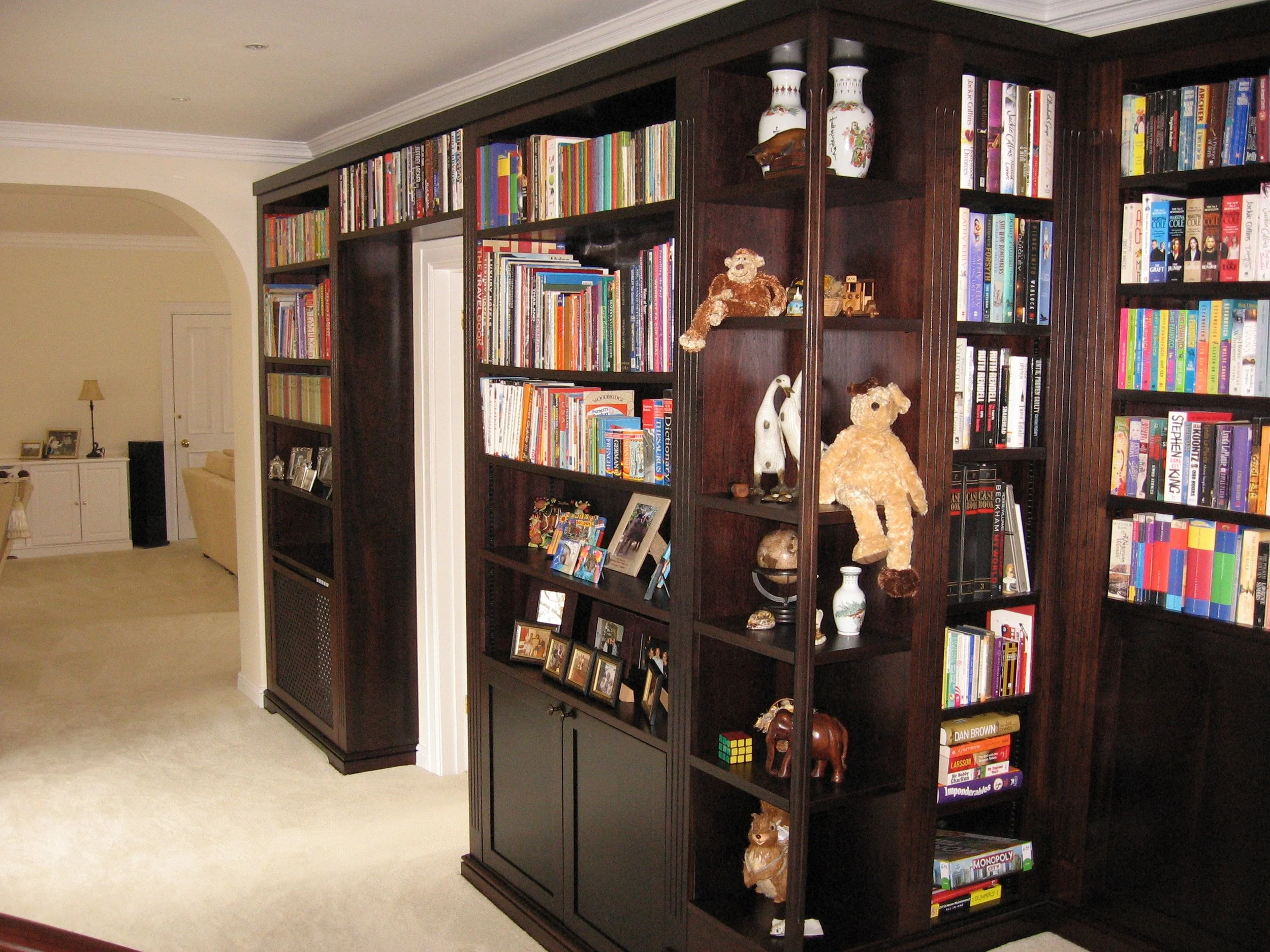 A dark wood bookshelf filled with books, toys, framed photos, and decorative items in a living room.