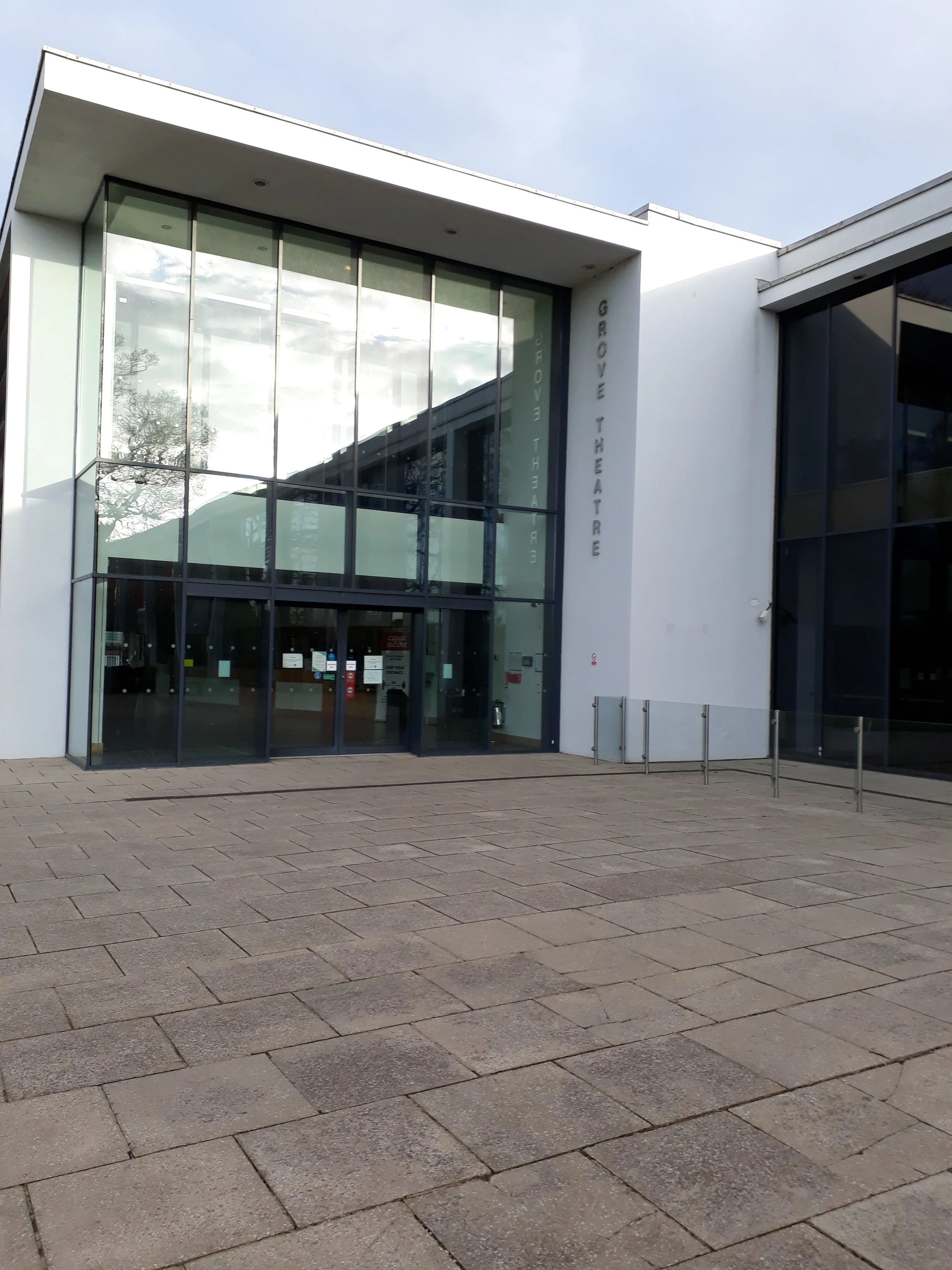 Exterior of a modern theater with large glass entrance, white walls, and paved walkway.