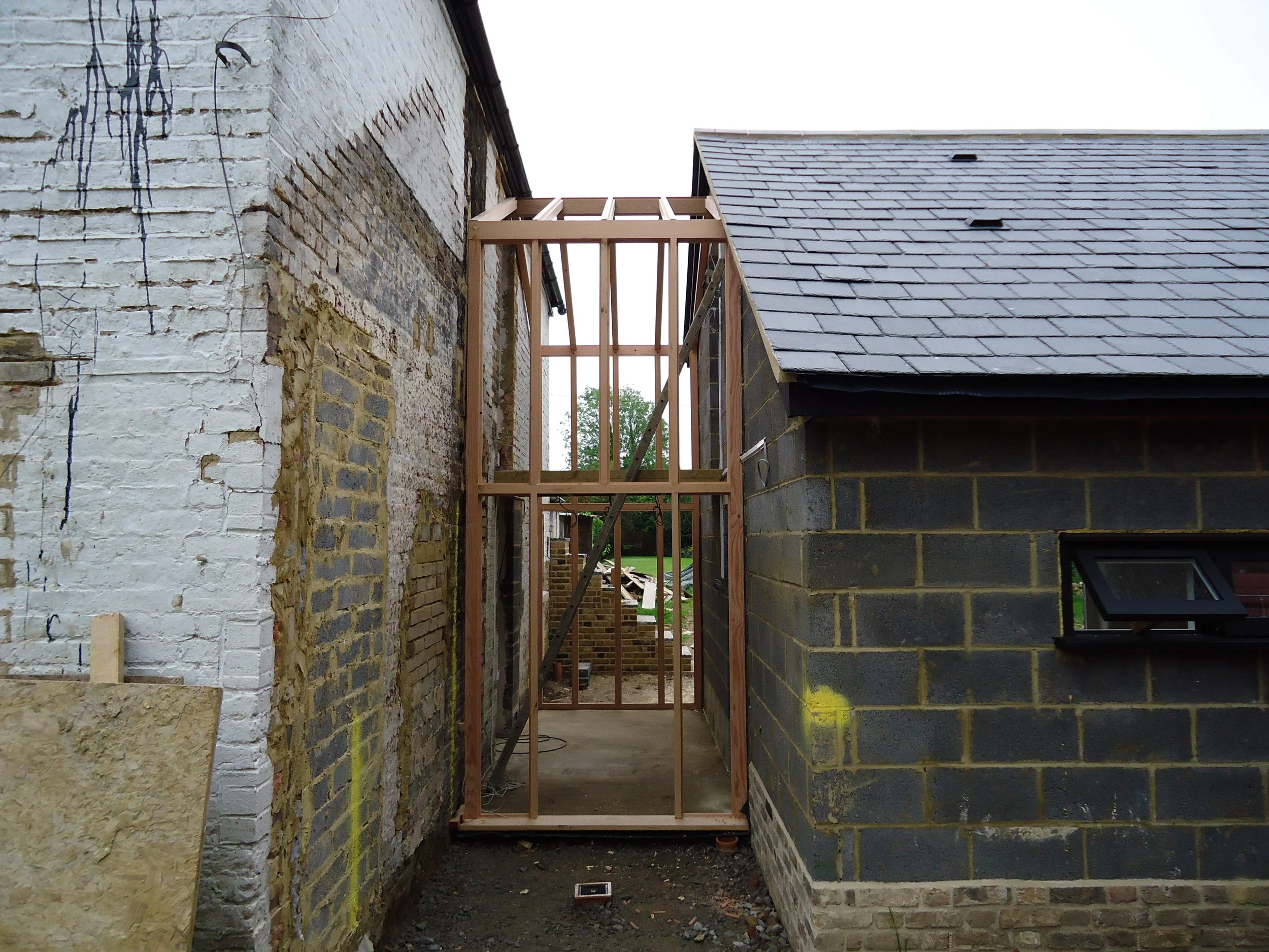 Construction site showing a wooden frame being built between two older brick and brick or stone structures.