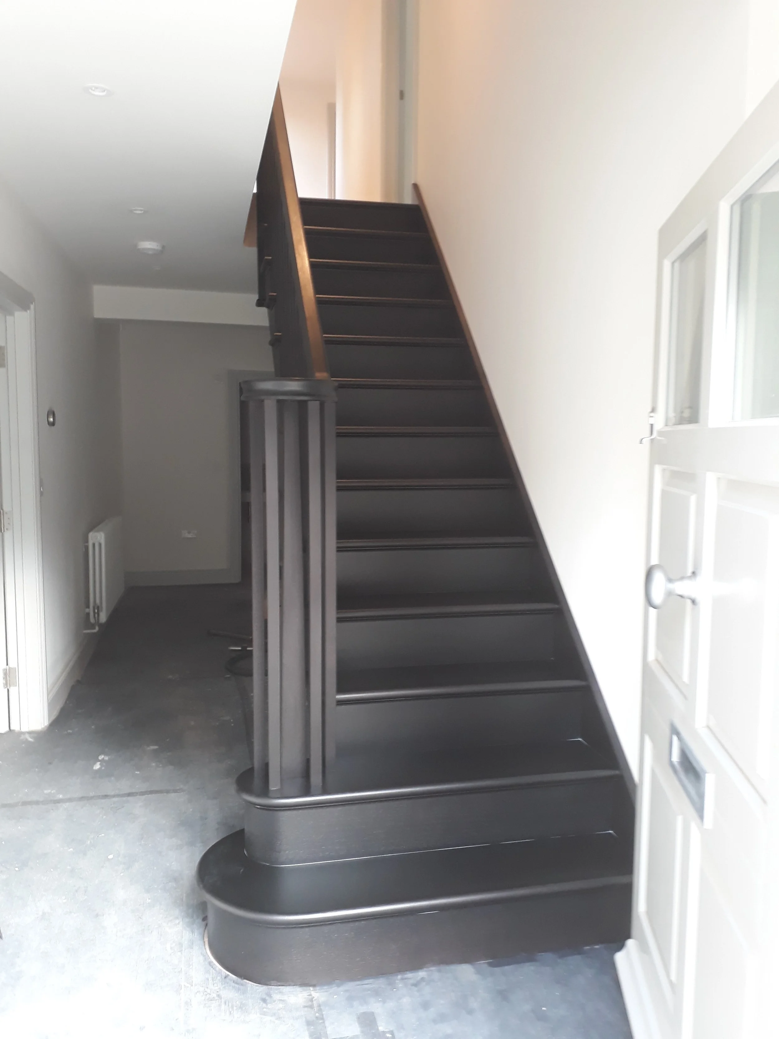 Black staircase with curved bottom landing inside a house, next to a white door with glass panels.