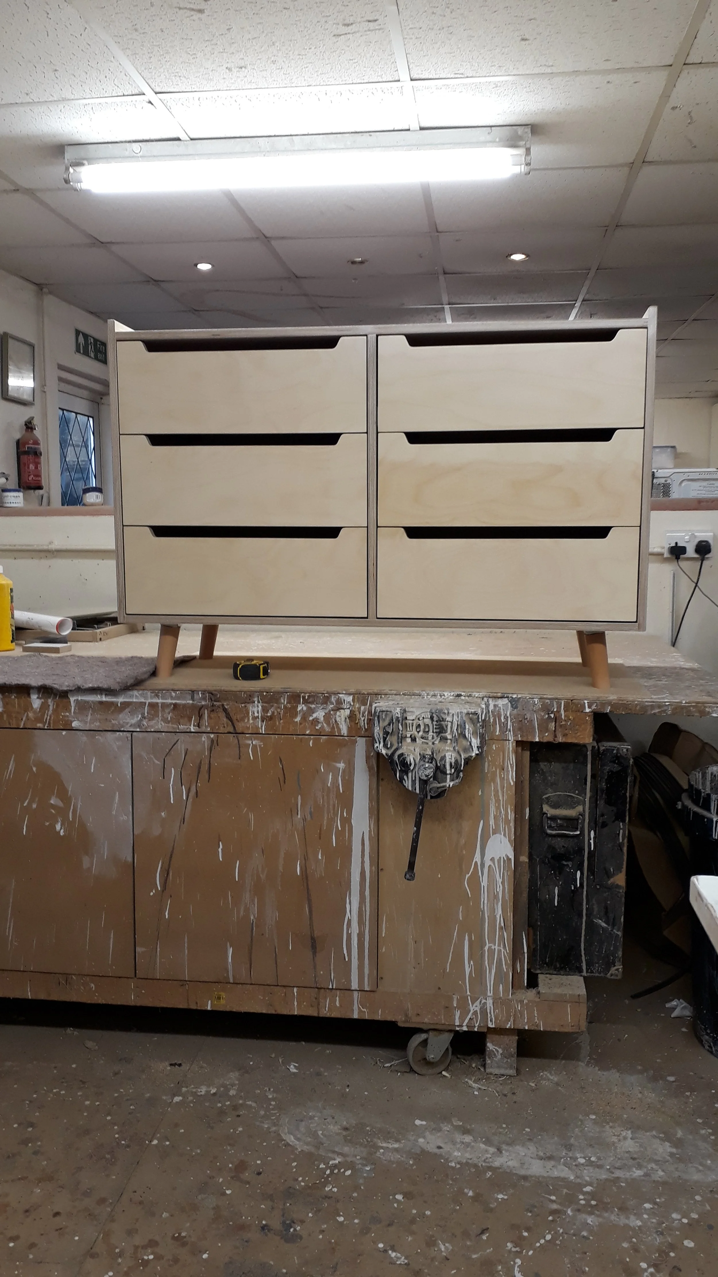 Unfinished wooden cabinet with six drawers on a workbench in woodworking shop.