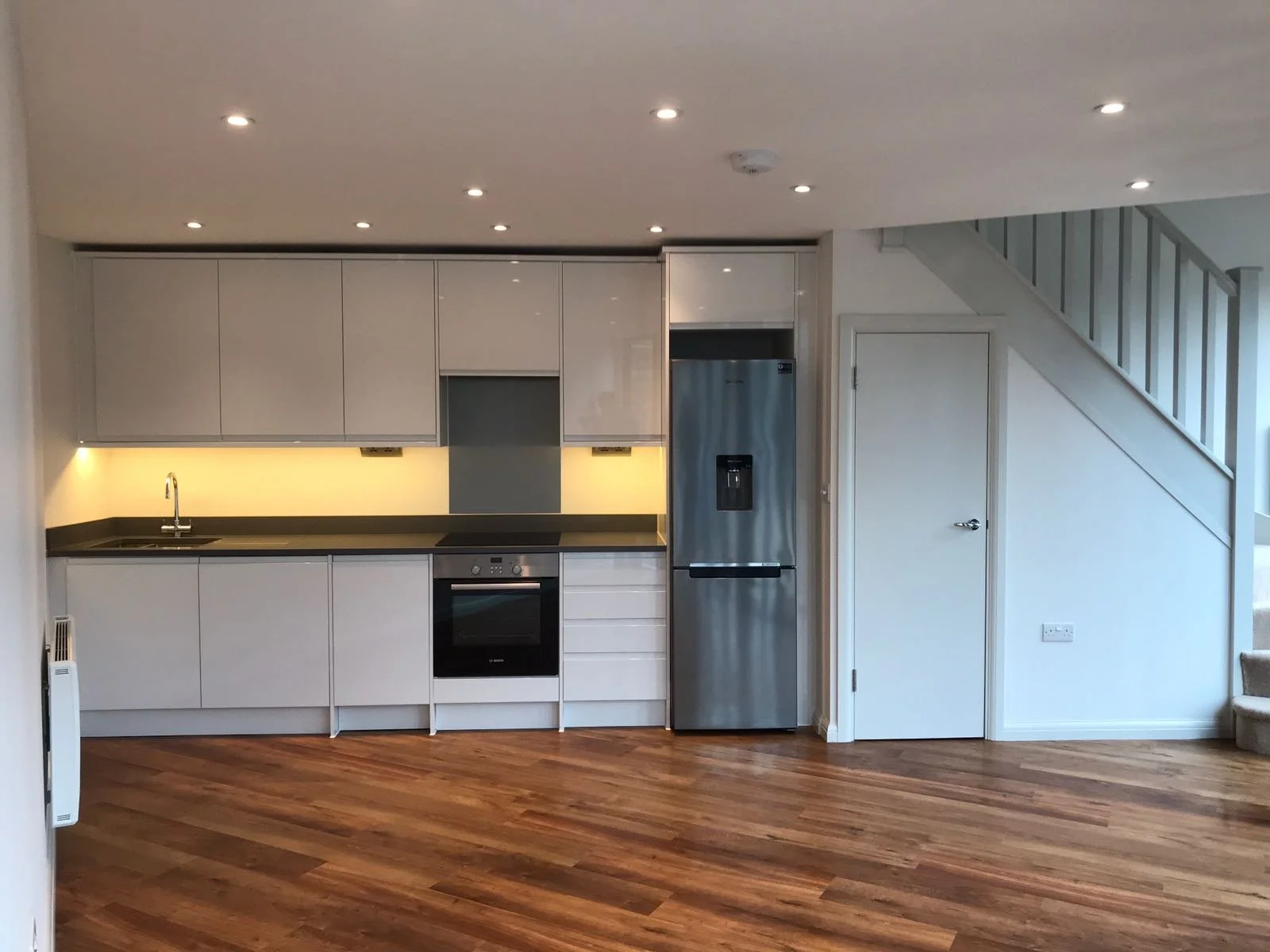 Modern kitchen with white cabinets, black countertop, stainless steel refrigerator, oven, and a staircase to the right.