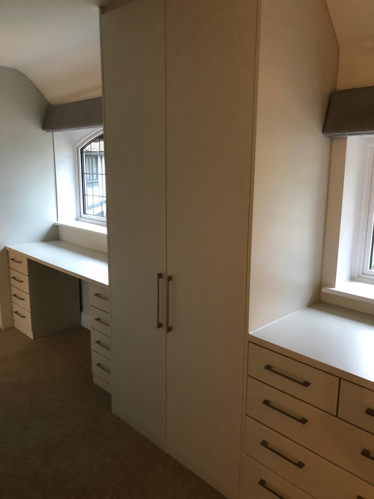 Interior view of a room with white built-in cabinets, drawers, and a desk under a window with natural light.