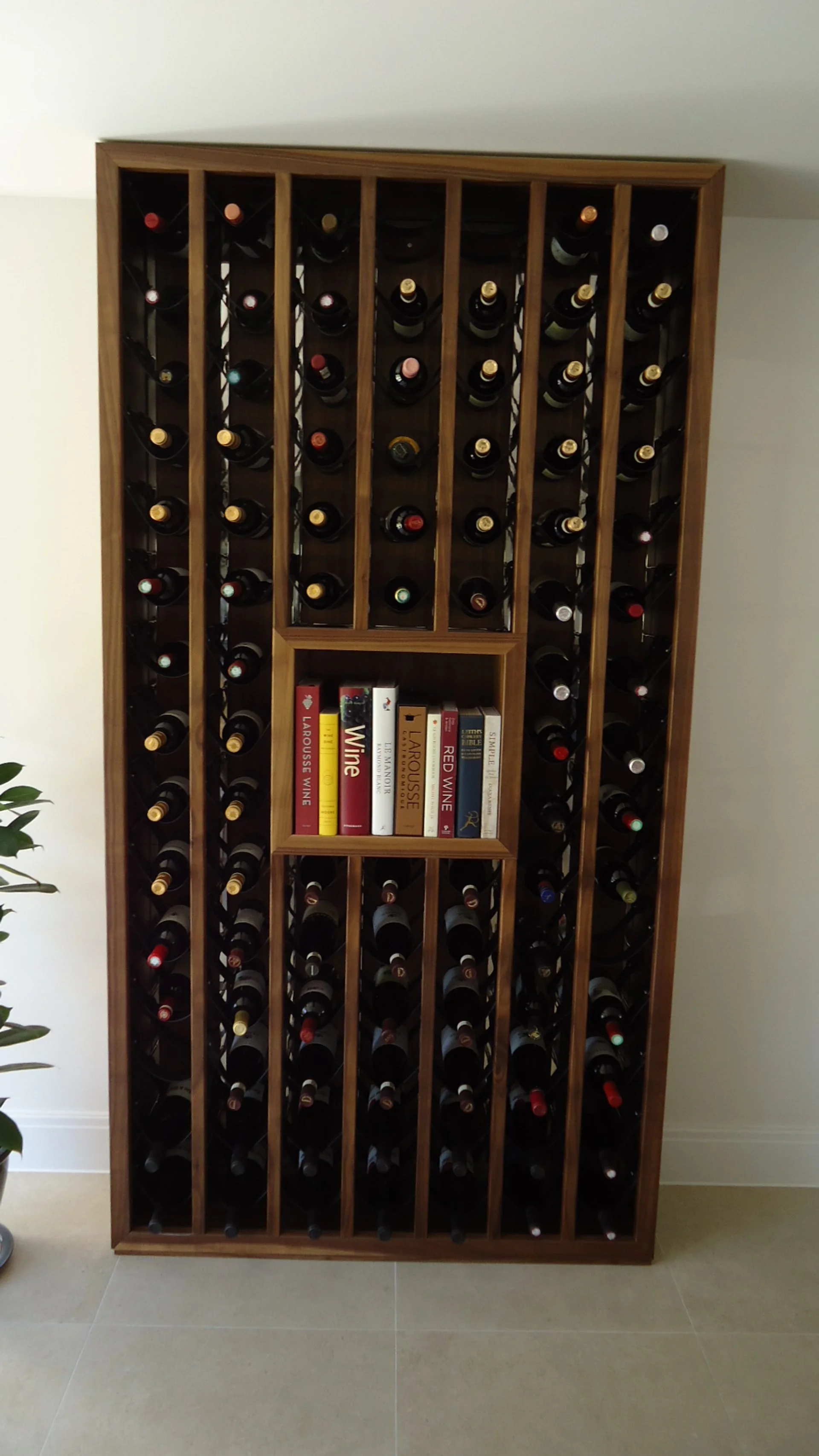 Wooden wine rack filled with wine bottles and a small central shelf holding books about wine.