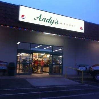 Exterior of Andy's Market store at dusk with a lit sign and glass doors showing inside shoppers.