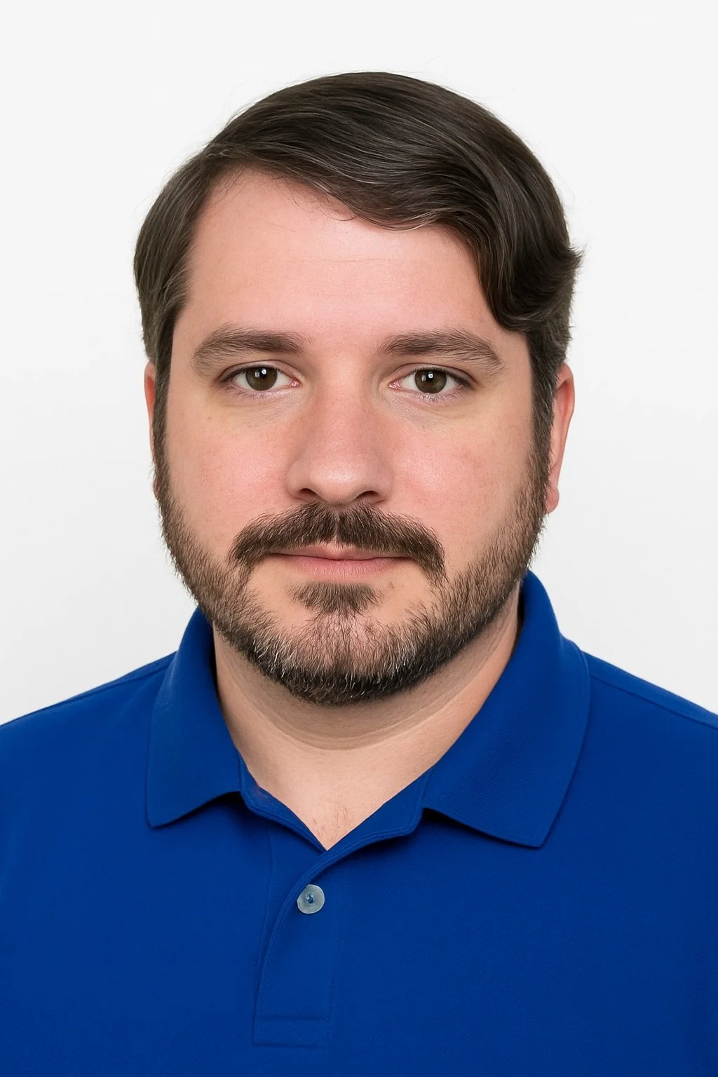 A man with brown hair, brown eyes, and a beard wearing a blue collared shirt against a white background.