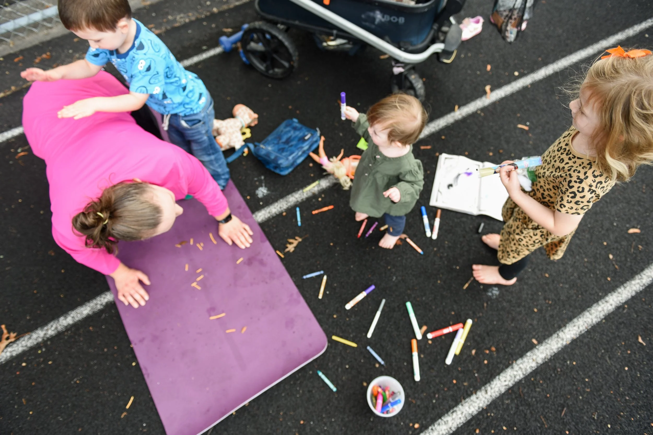 Children from the SouthCoast playing with colored markers at Cushman Park in Fairhaven during an iStroll Southcoast class near a stroller and purple yoga mat.