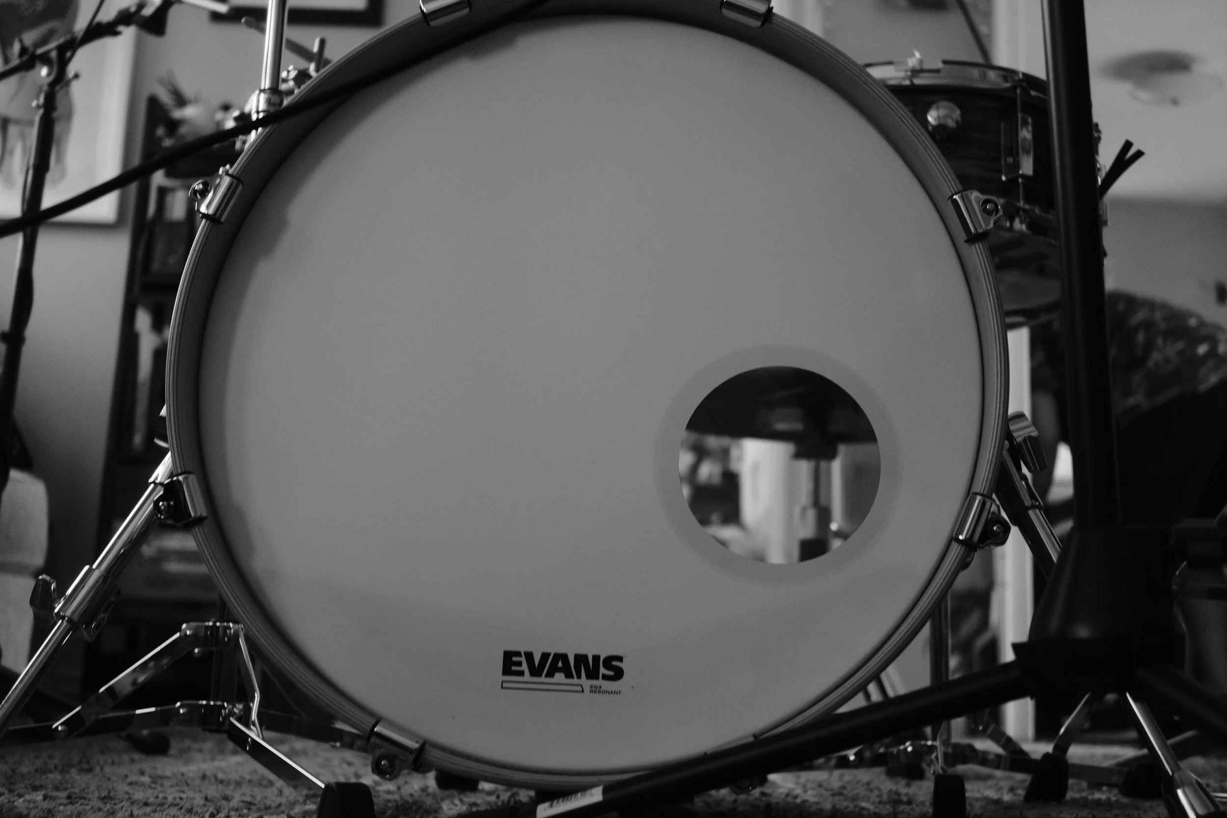 Black and white photo of an Evans bass drum with a reflective surface, part of a drum set, in a room with shelves and picture frames in the background.