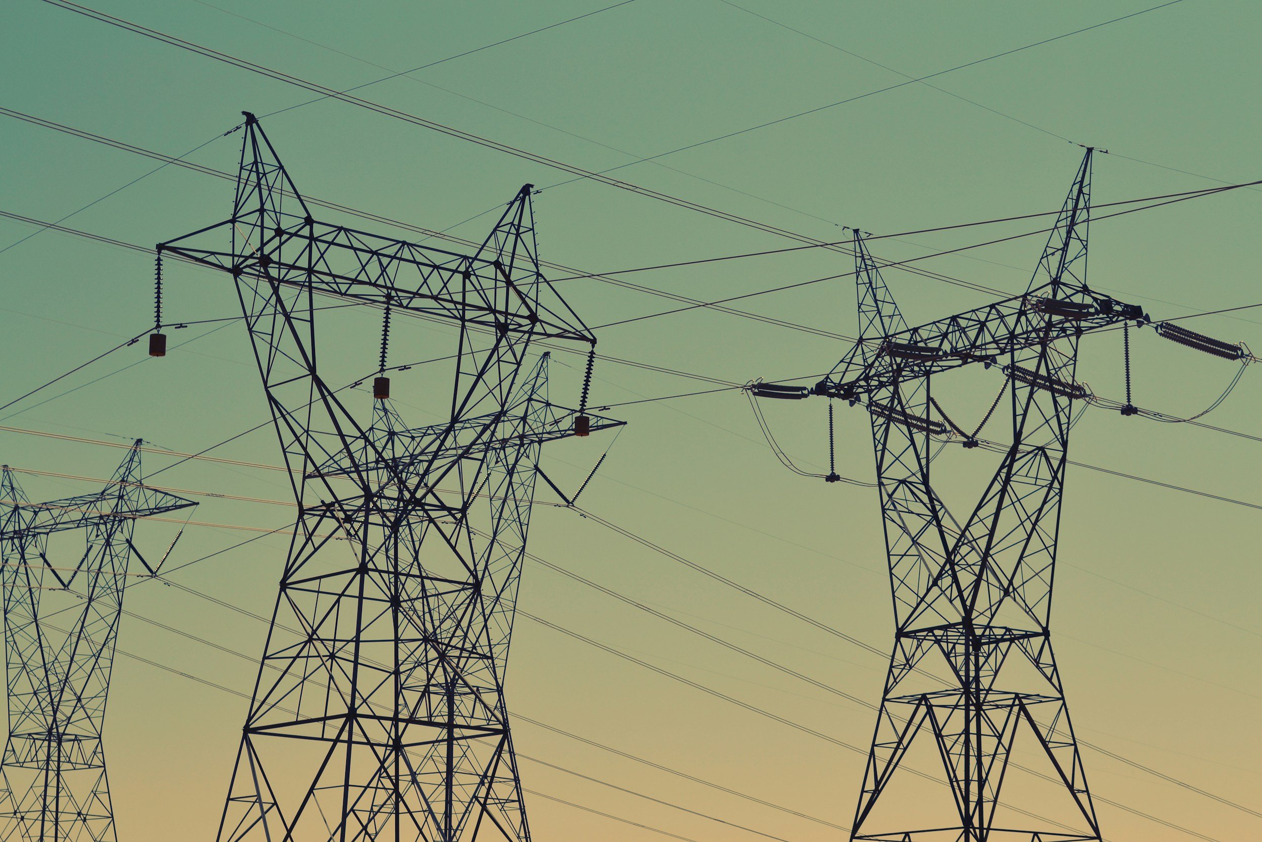 Electric power transmission towers with power lines against a gradient sky.