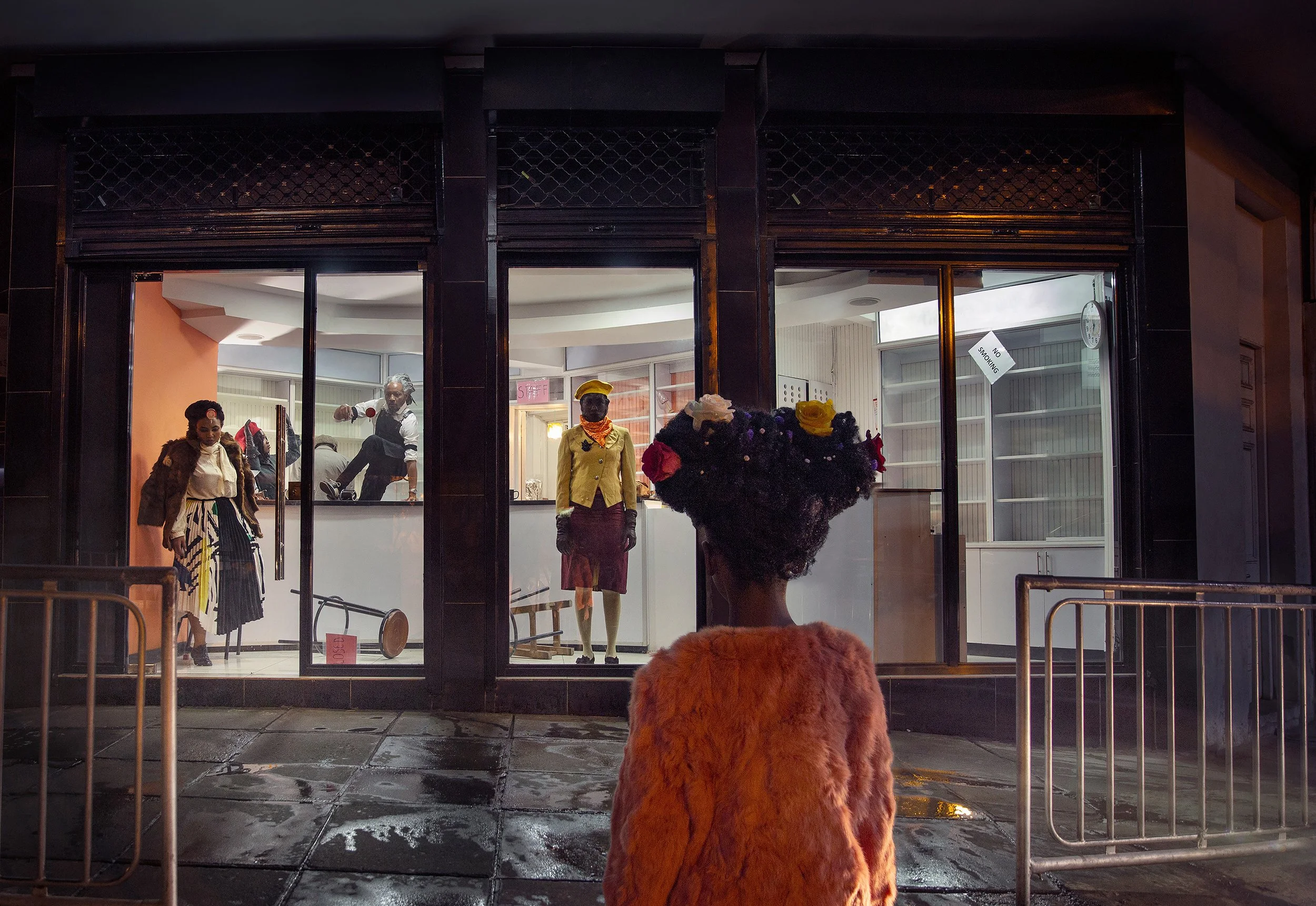 A person dressed in a fuzzy orange costume standing outside at night, looking into a clothing store window with mannequins wearing fashionable outfits indoors.