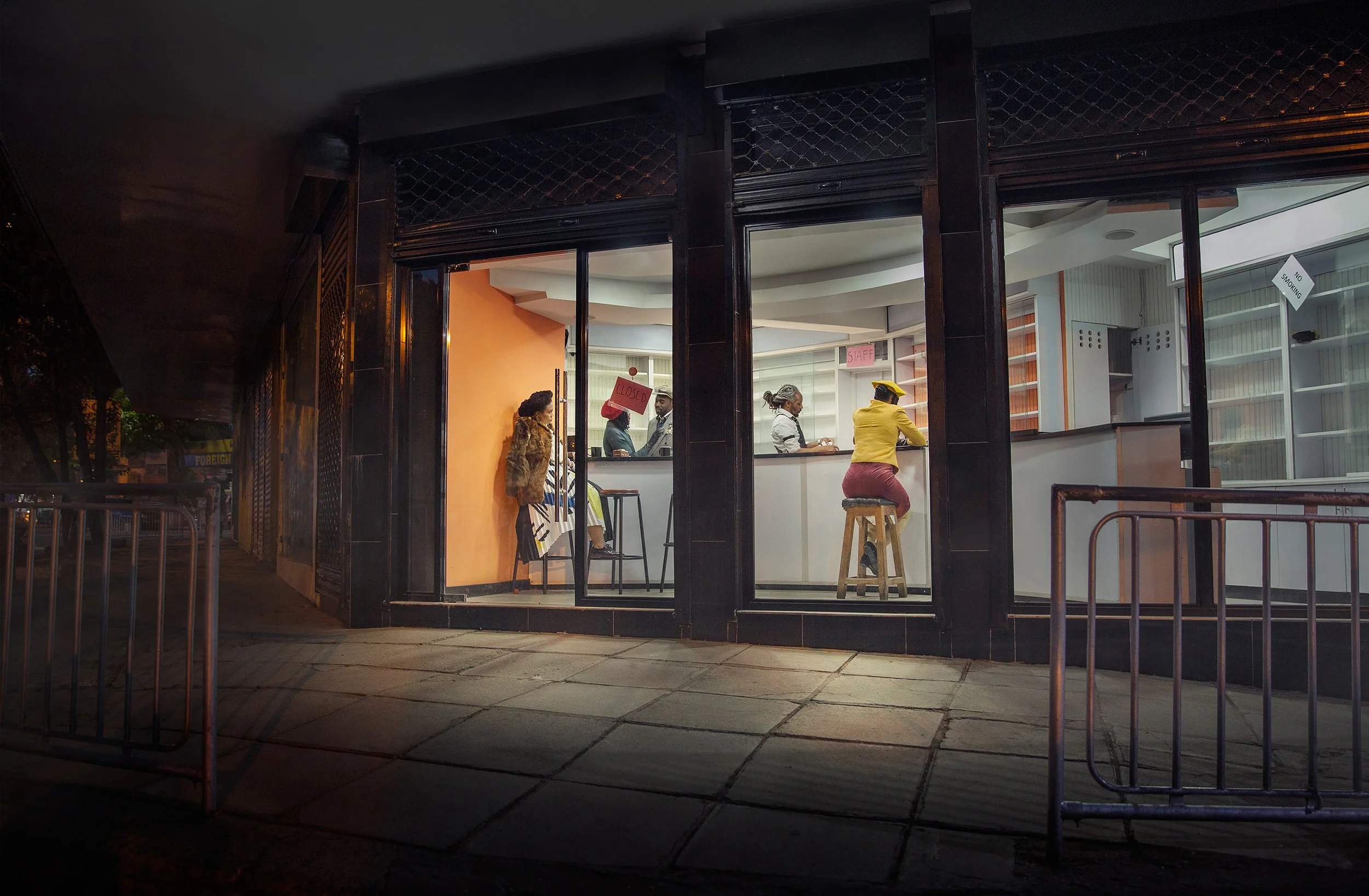 Nighttime view of a closed fast food restaurant with a visible sign on the door that says 'Closed,' and staff inside working at the counter.