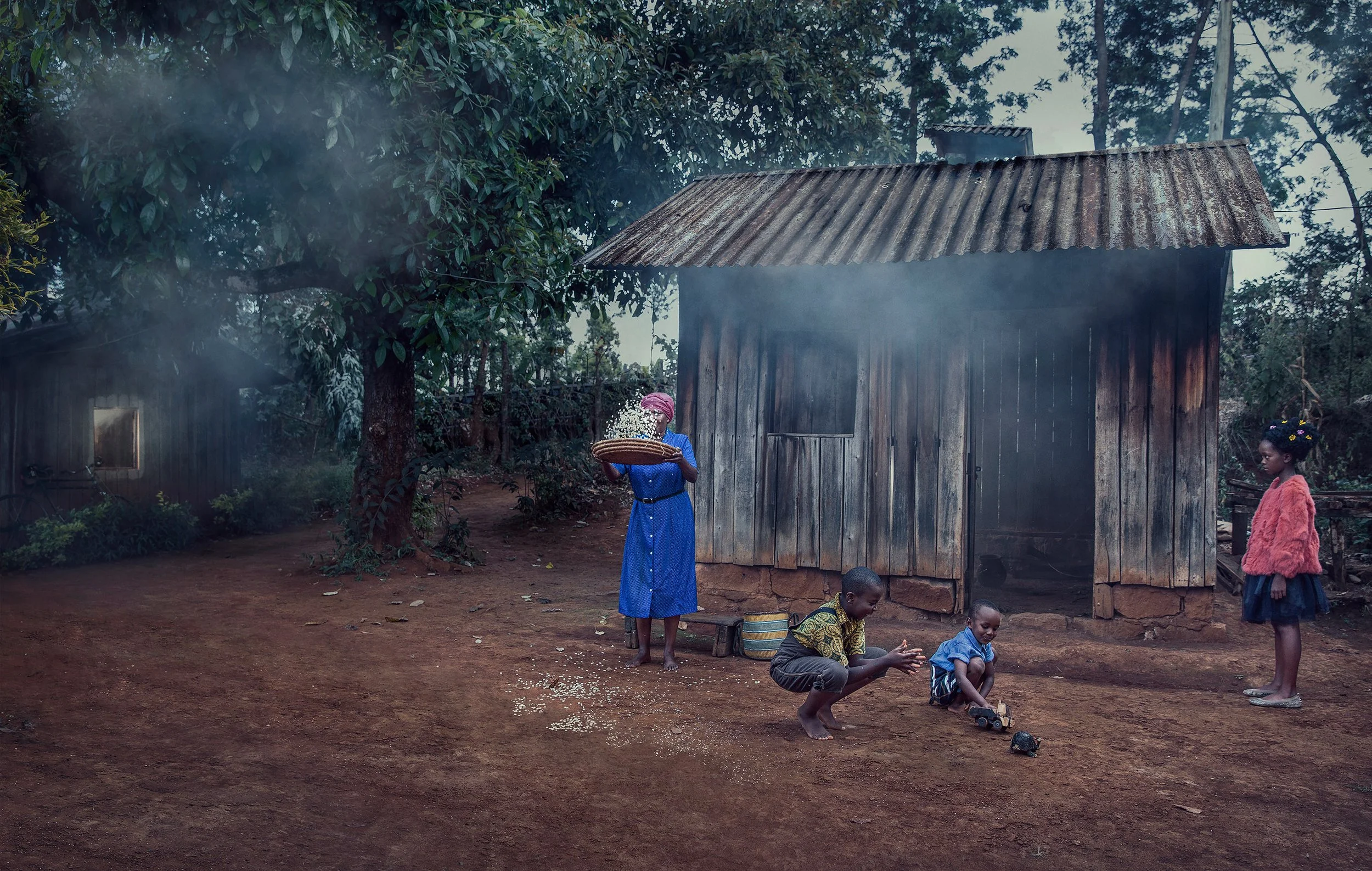 Children playing outside near wooden houses and trees in a rural setting, with some children squatting and a woman standing holding a basket.